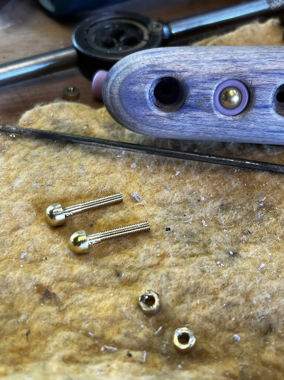 Outils et pièces en métal, notamment deux vis en or, sur une surface en feutre ou isolant, avec un objet en bois ou en plastique avec des trous