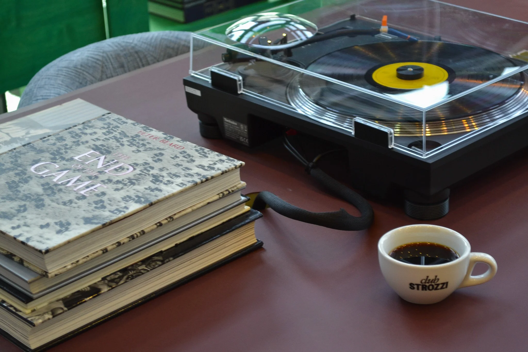 A table with a vinyl record player, a stack of books, and a white coffee mug with black coffee. The mug has the text 'club STROZZI' on it.