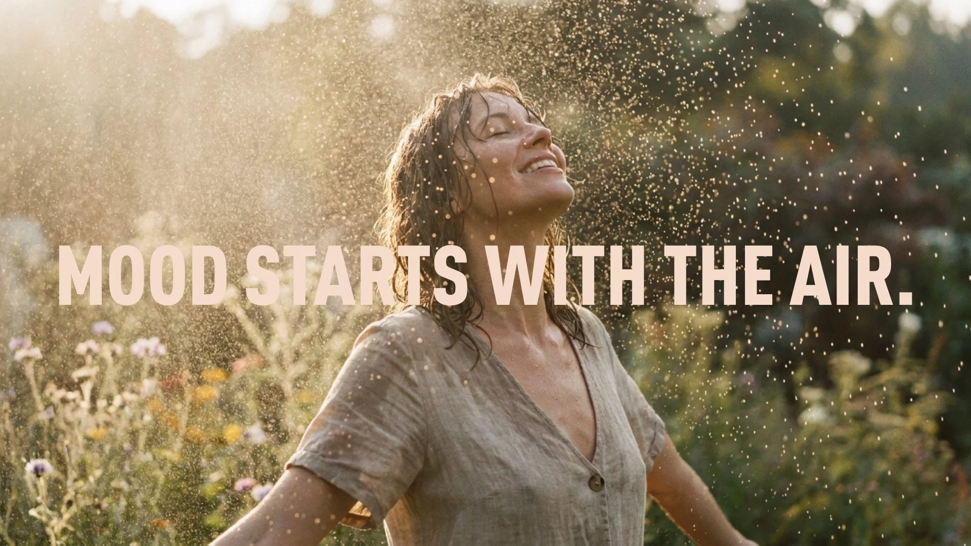 Vrouw met nat haar die lacht en in de zon staat, omgeven door bloemen en stofdeeltjes in de lucht, met de tekst 'MooD starts with the air' bovenaan.