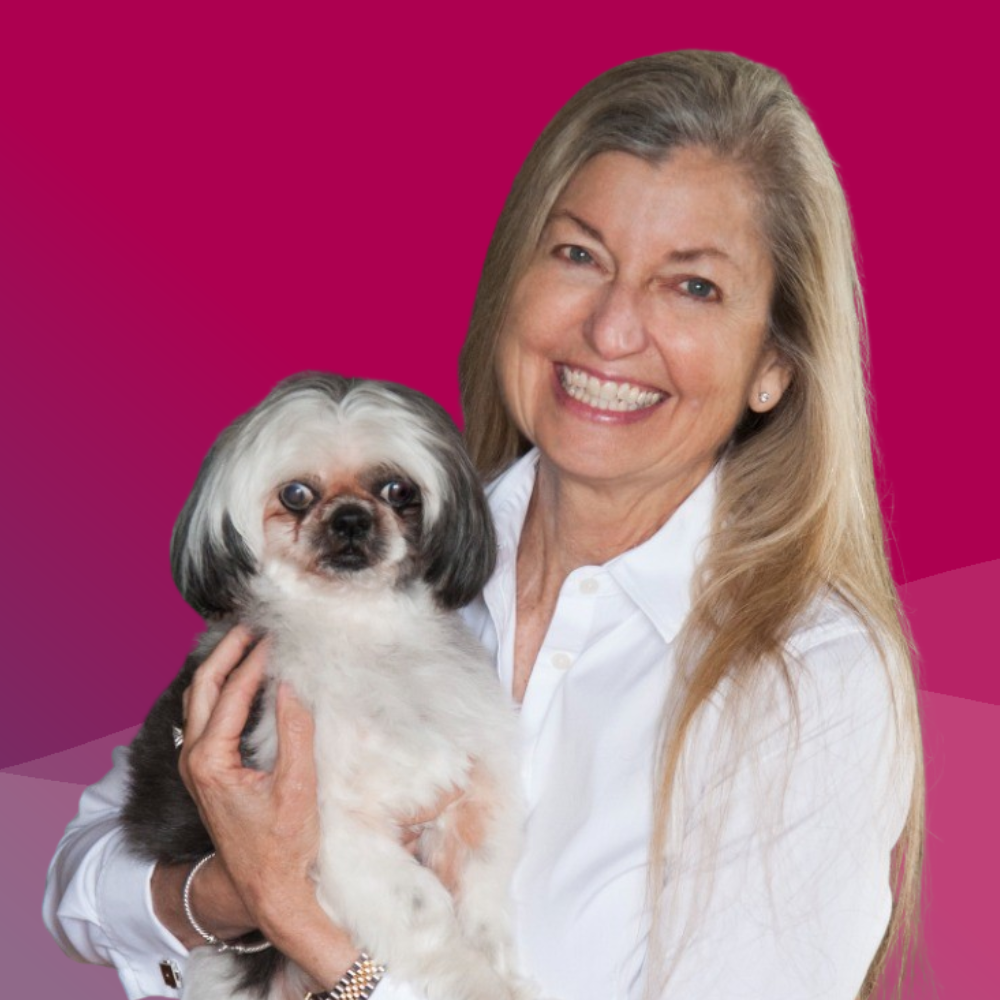Smiling woman holding a small dog in front of a pink background.