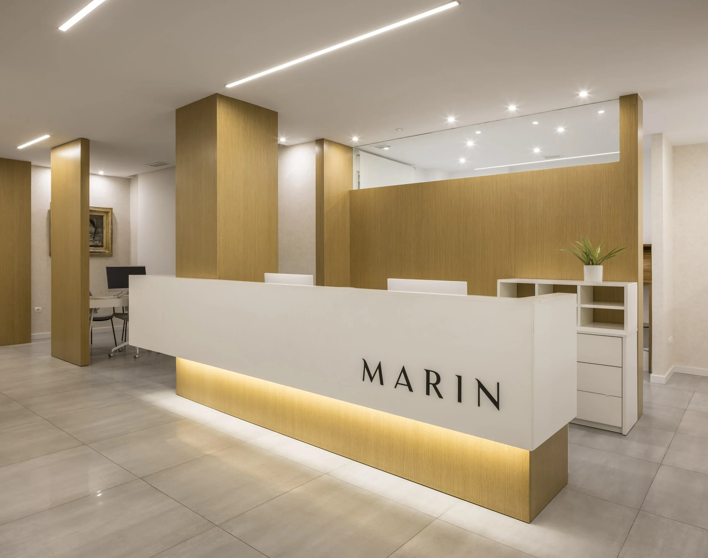 Mostrador en una oficina de diseño o recepción con un cartel que dice 'MARIN' en letras negras, paredes blancas, columnas de madera y plantas decorativas.