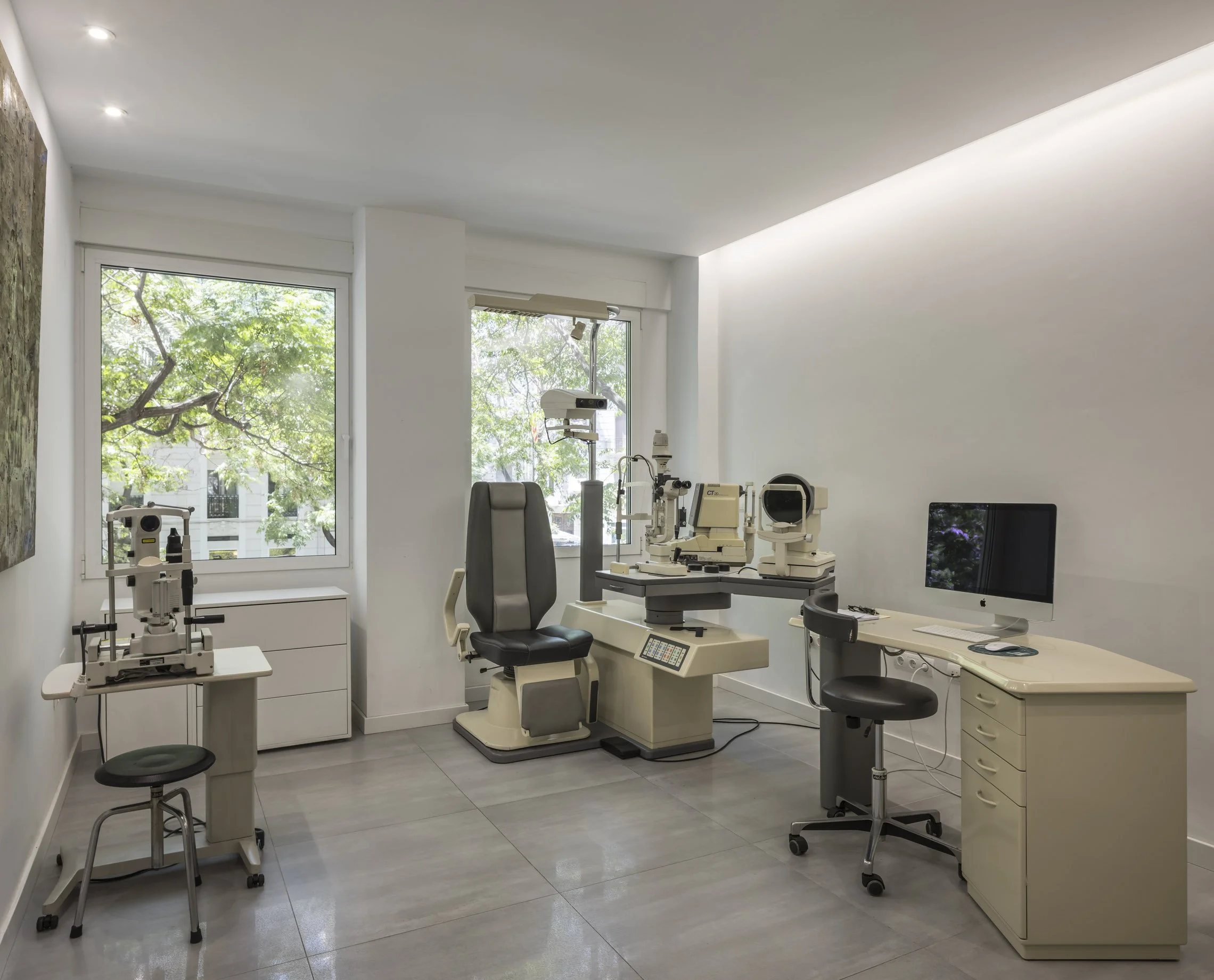 Consulta médica con equipos oftalmológicos y una silla en una clínica moderna con ventanas grandes
