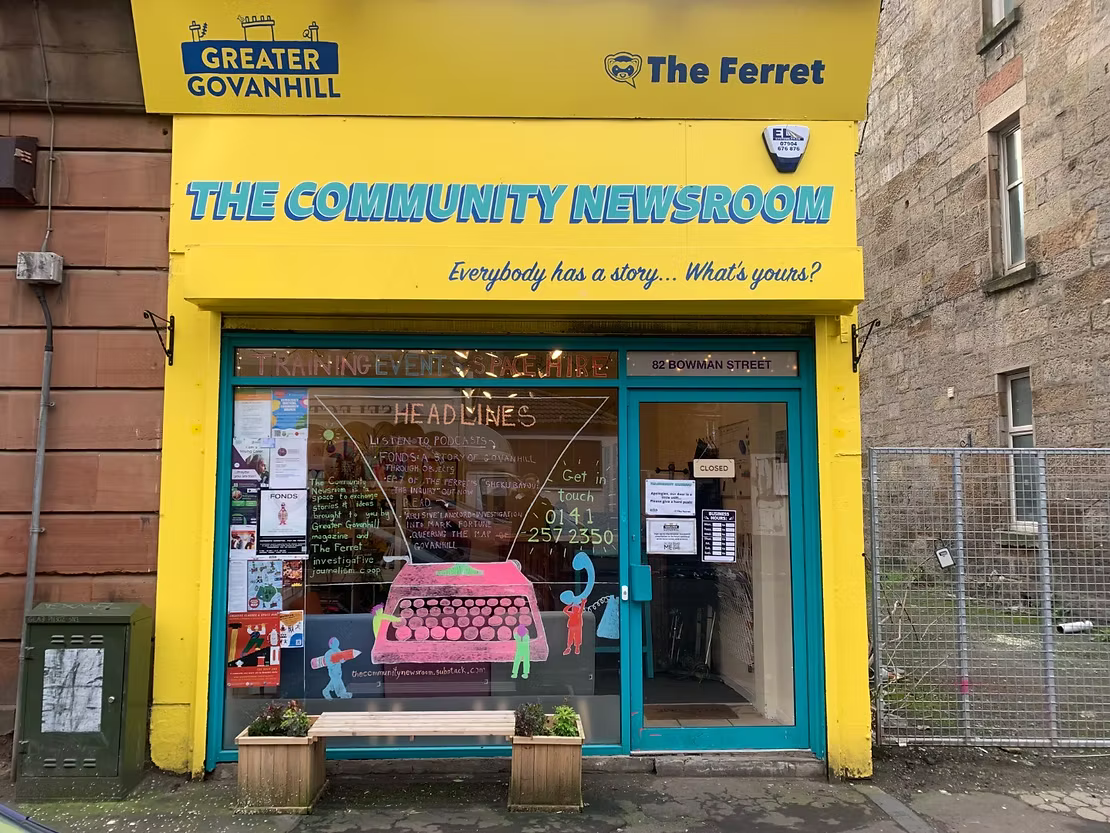 A photo of a bright yellow shopfront on a high street, with the words 'THE COMMUNITY NEWSROOM' above it. Below, in smaller writing, are the words 'Everybody has a story... What's yours?'