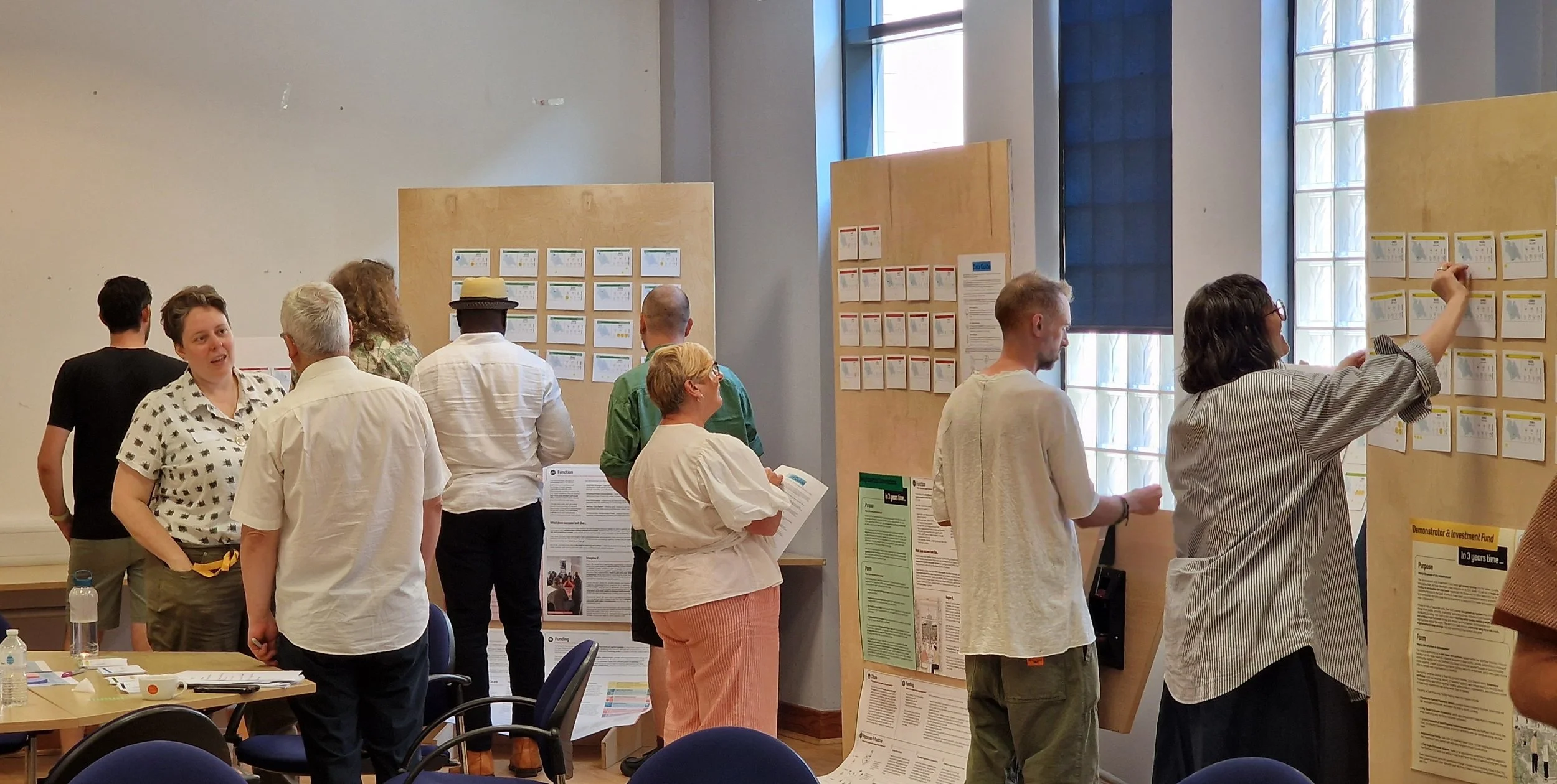 A photo of about a dozen standing in a room, looking at information on vertical display boards