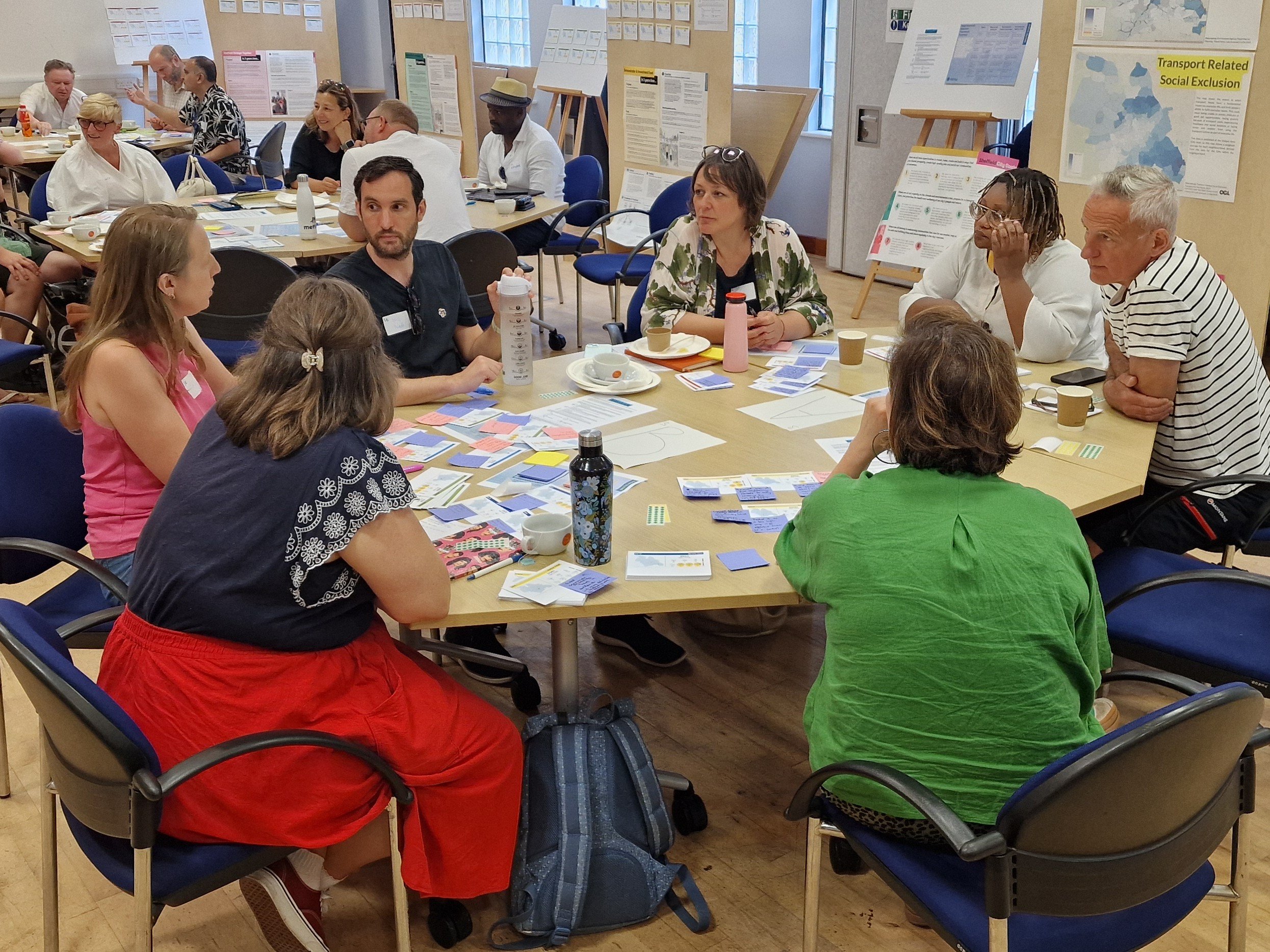 A photo of seven people chatting in a roundtable discussion, with post-its and pieces of paper all over the table