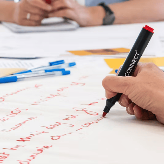A photo of someone's hand writing on a large sheet of paper in red marker.
