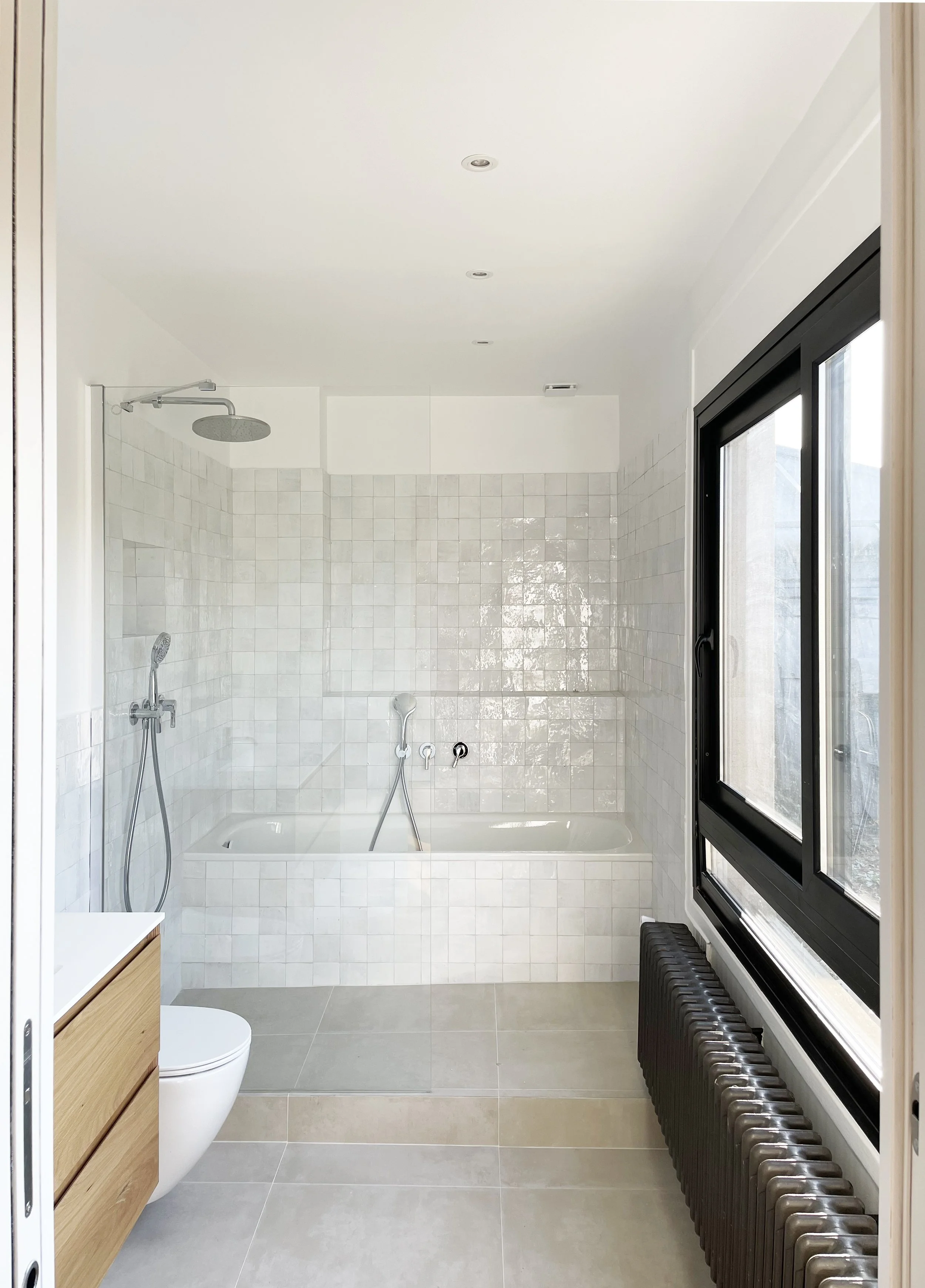 Salle de bain moderne avec baignoire, douche à l'italienne, fenêtre noire, radiateur noir et lavabo en bois.