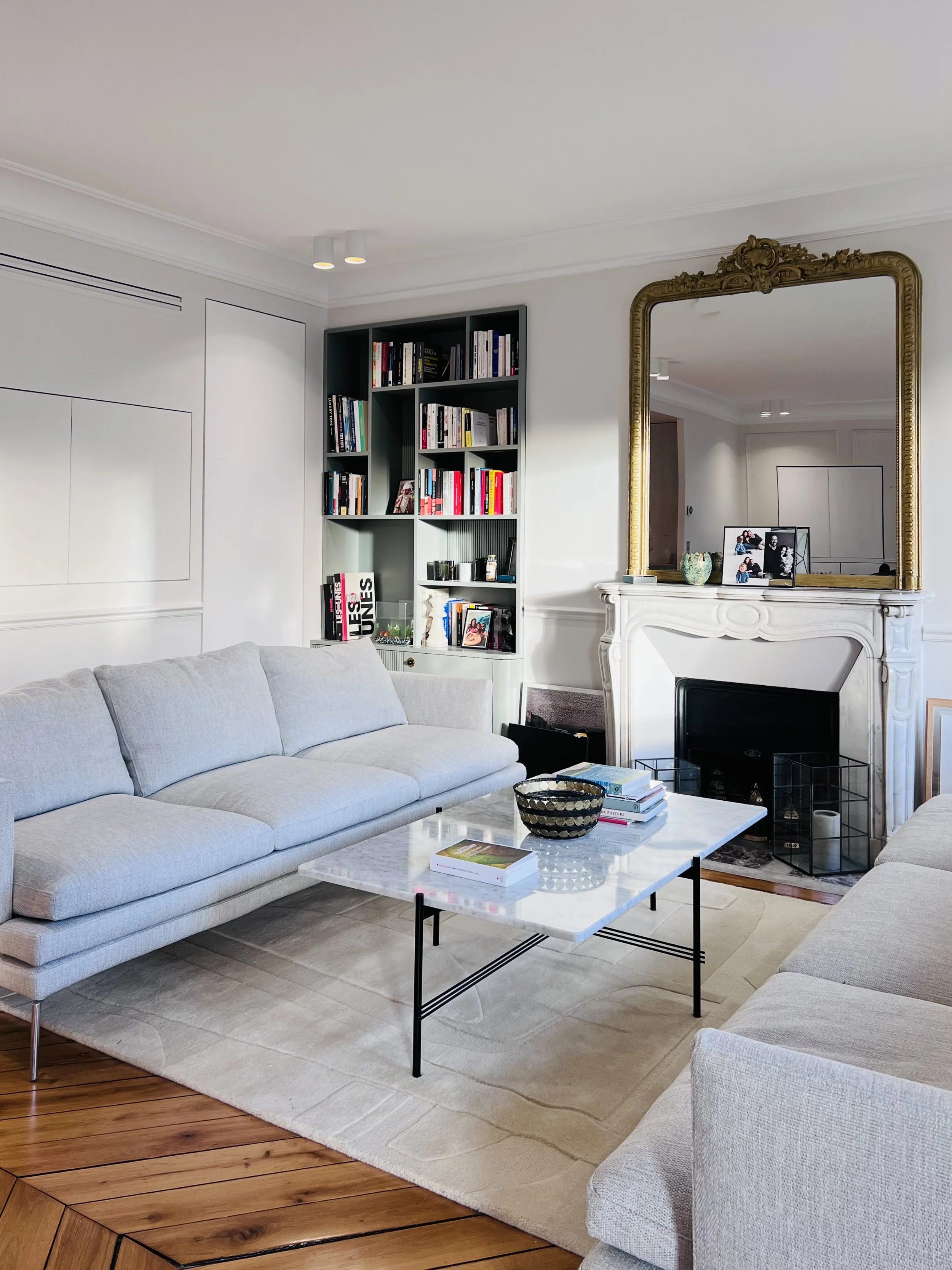 Cuisine moderne avec une table blanche et six chaises blanches autour, armoires blanches, parquet en bois, grande fenêtre avec rideaux, luminaire suspendu.