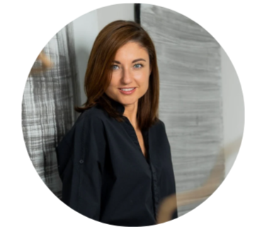 Portrait of a woman with shoulder-length brown hair, wearing a navy blue shirt, standing against a textured gray background.