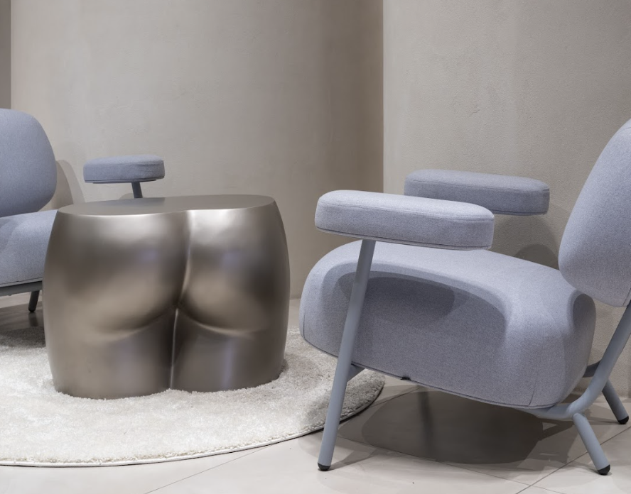 Modern living room with a metallic stool-shaped side table, light gray upholstered chairs, and a round white rug