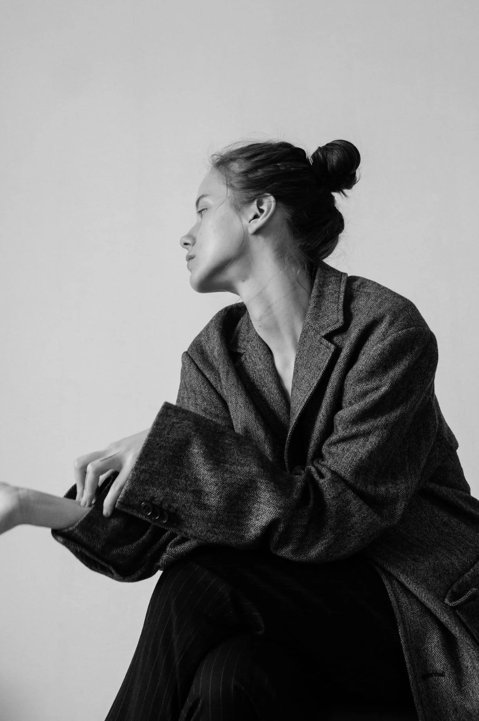 A woman with her hair in a bun, wearing a blazer, sitting with her eyes closed, and holding someone's hand.