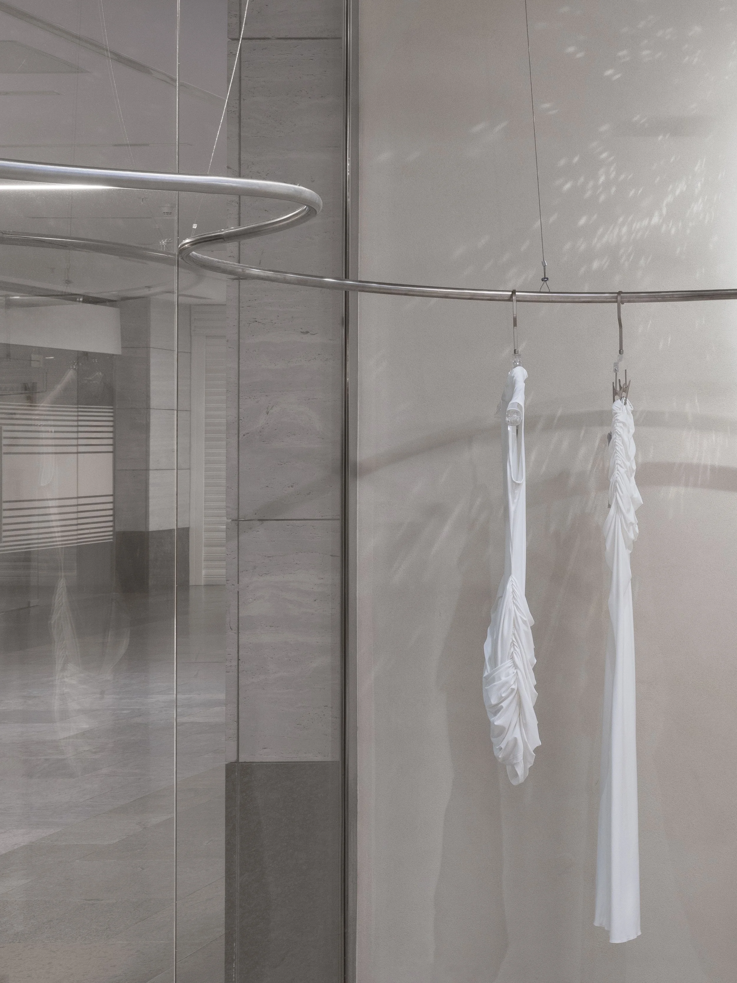 Two white fabric umbrellas hanging from a curved metal rod in a modern, minimalist space with light-colored walls and floor.