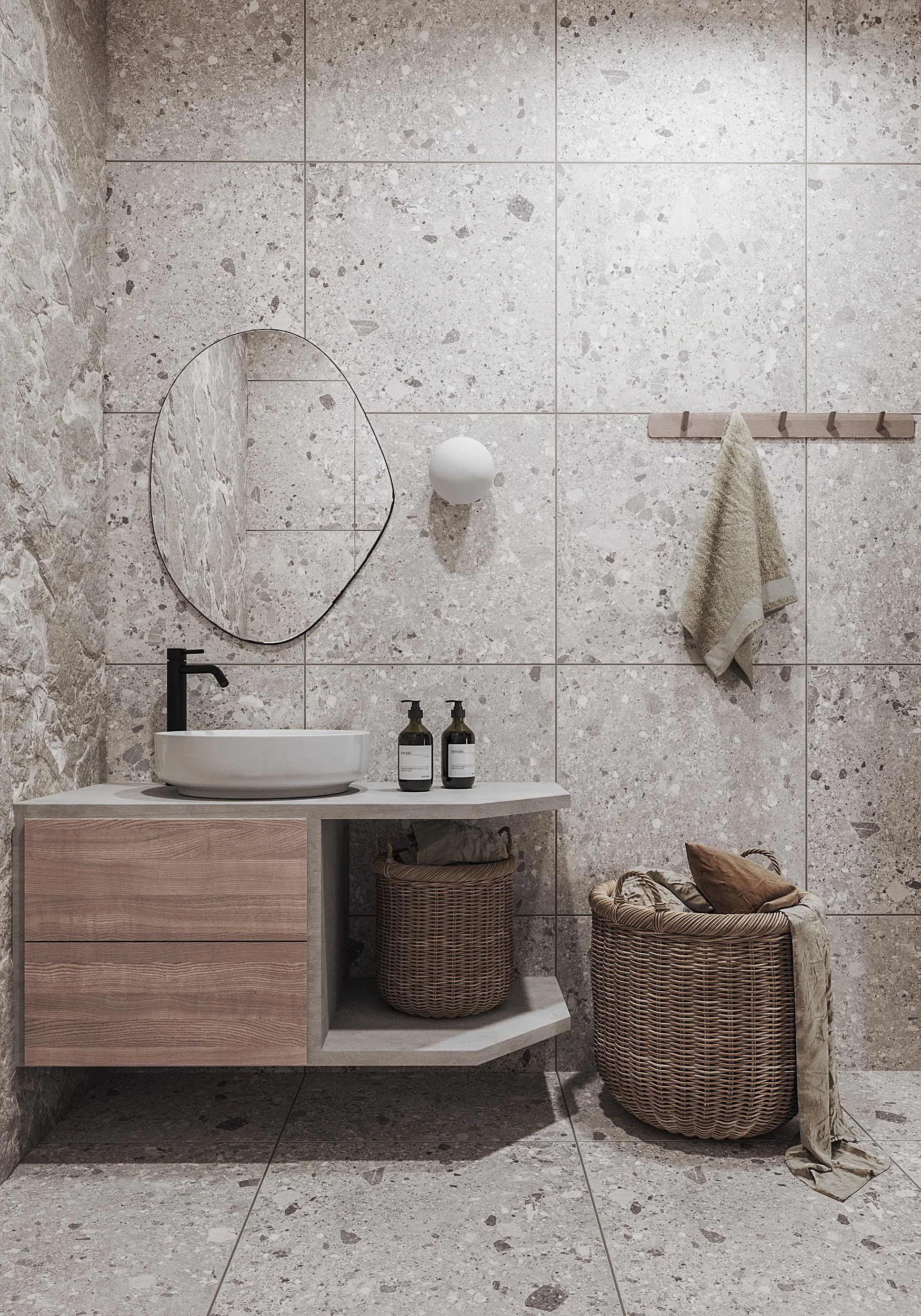 A minimalist bathroom with a round mirror, a vessel sink, a black faucet, two soap dispensers, a woven basket, a wicker laundry basket, a hanging towel, and a wall-mounted wooden coat rack with hooks, all against a stone tile wall and floor.