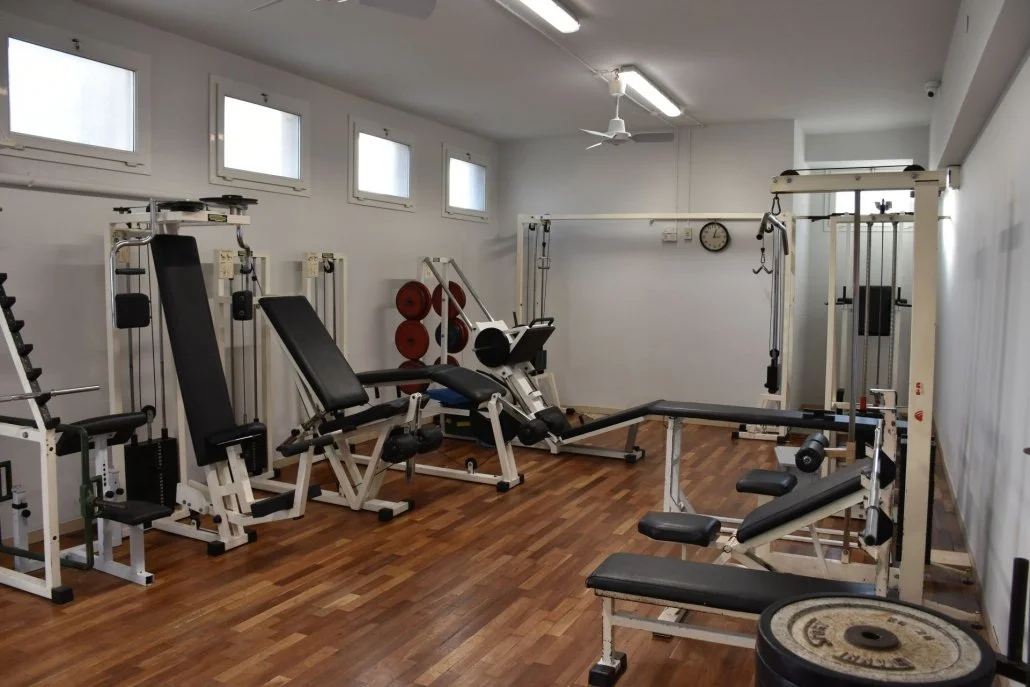 Sala fitness attrezzata con panche, pesi, macchinari da allenamento e un orologio sulla parete.