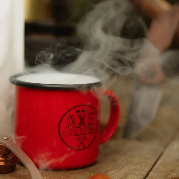 A red enamel mug with steaming hot beverage on a wooden surface.