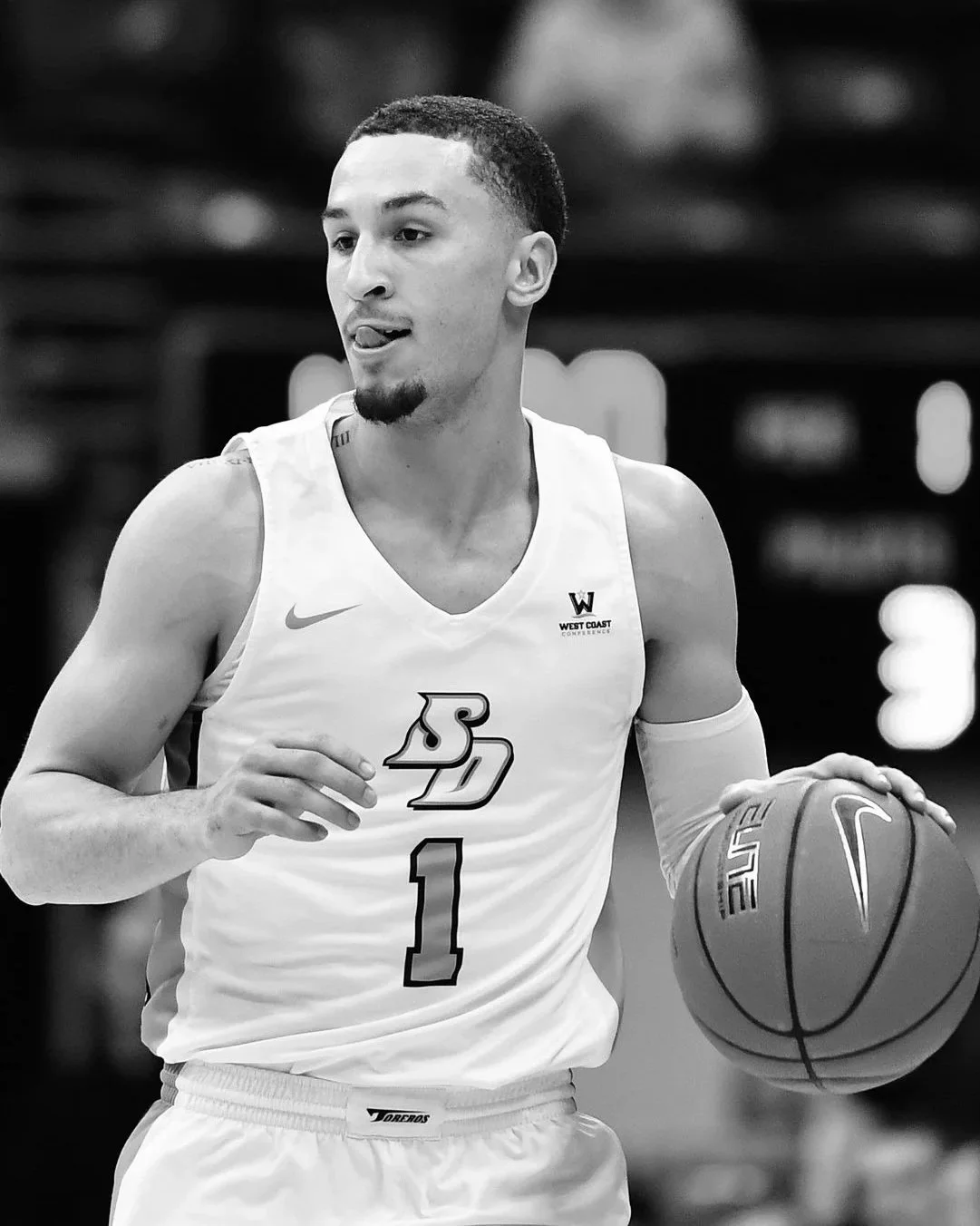 A male basketball player holding a basketball on a basketball court, wearing a uniform with the number 1 and a logo that says SD. The image is in black and white.