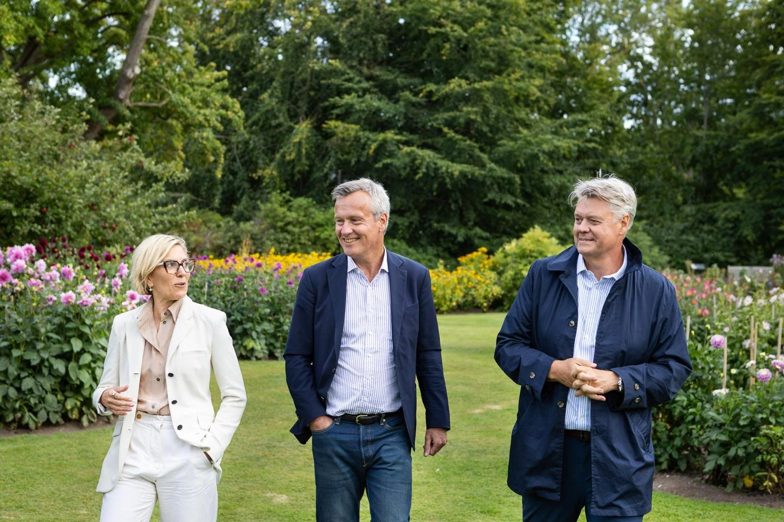 Eine Frau mit Brille sitzt auf einem modernen grauen Sofa in einem hell erleuchteten Raum, Blick nach vorne, im Hintergrund große Fenster mit Blick auf einen grünen Garten.