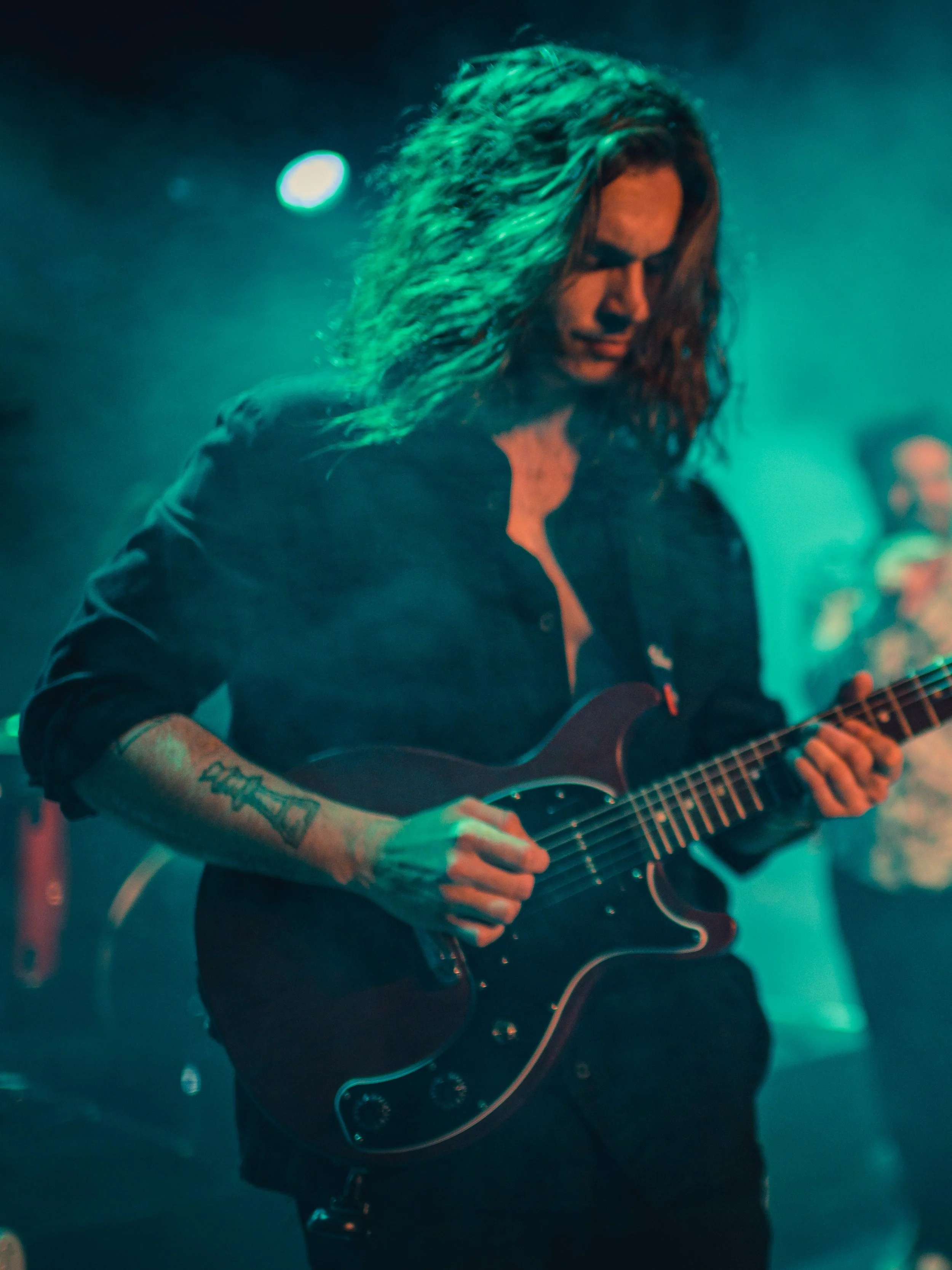 Jeune homme jouant de la guitare électrique dans un environnement de concert avec éclairage coloré.