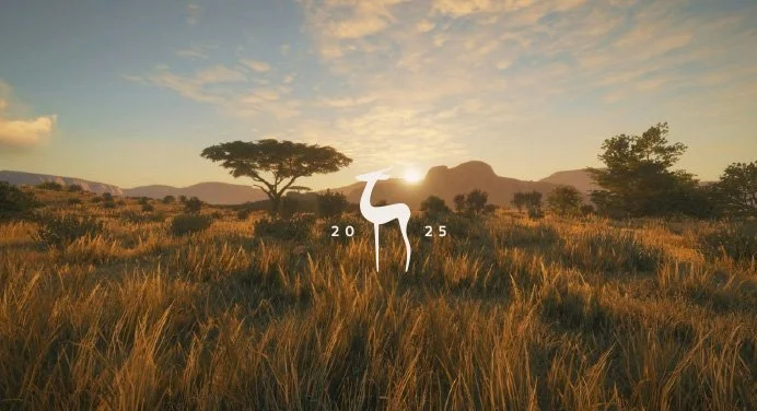 Sunset over wide savannah with tall grasses, a few trees, and distant mountains, featuring a white stylized antelope graphic with the year 2025.
