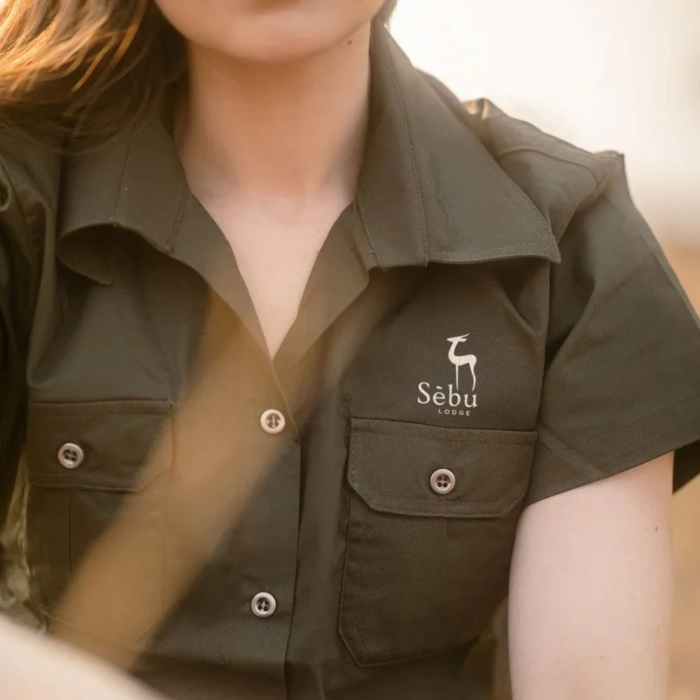 Close-up of a woman wearing a dark green shirt with the logo and text 'Sebu Lodge' on the chest, featuring a small deer icon.