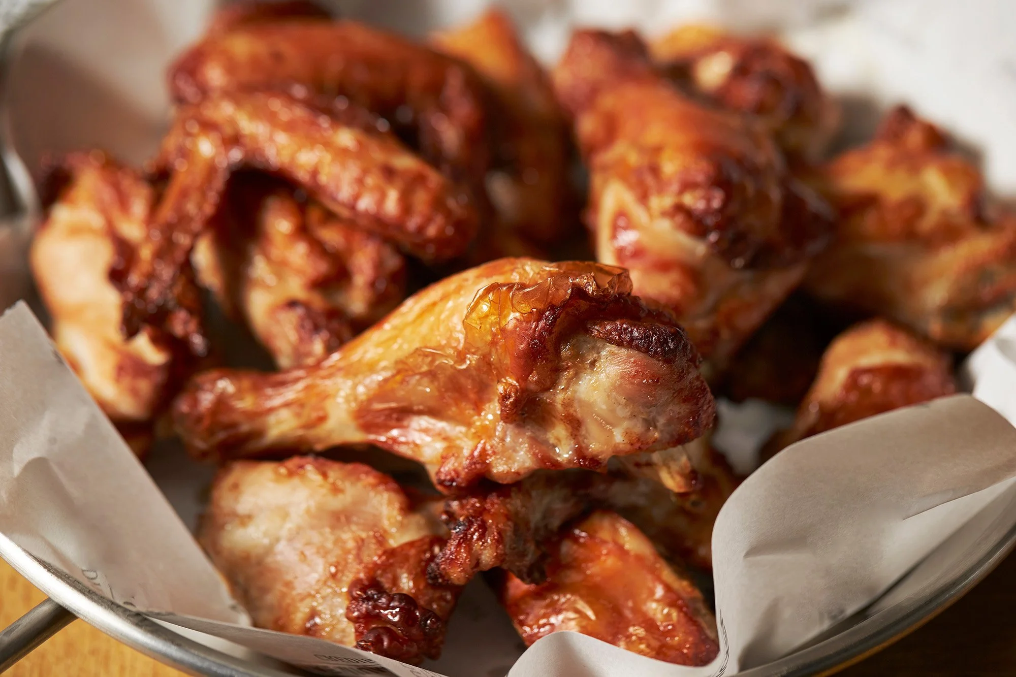 Close-up of cooked chicken wings in a basket lined with white paper.
