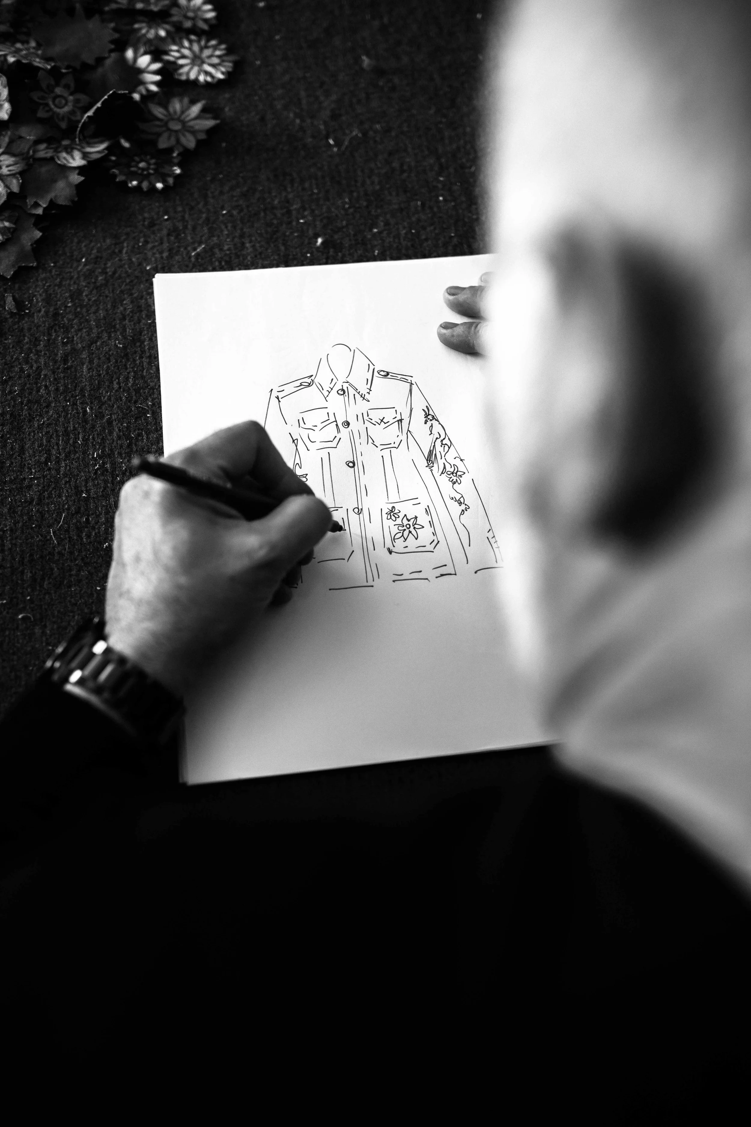 Una persona disegna un abito con motivi a fiori su un foglio, vista da sopra.