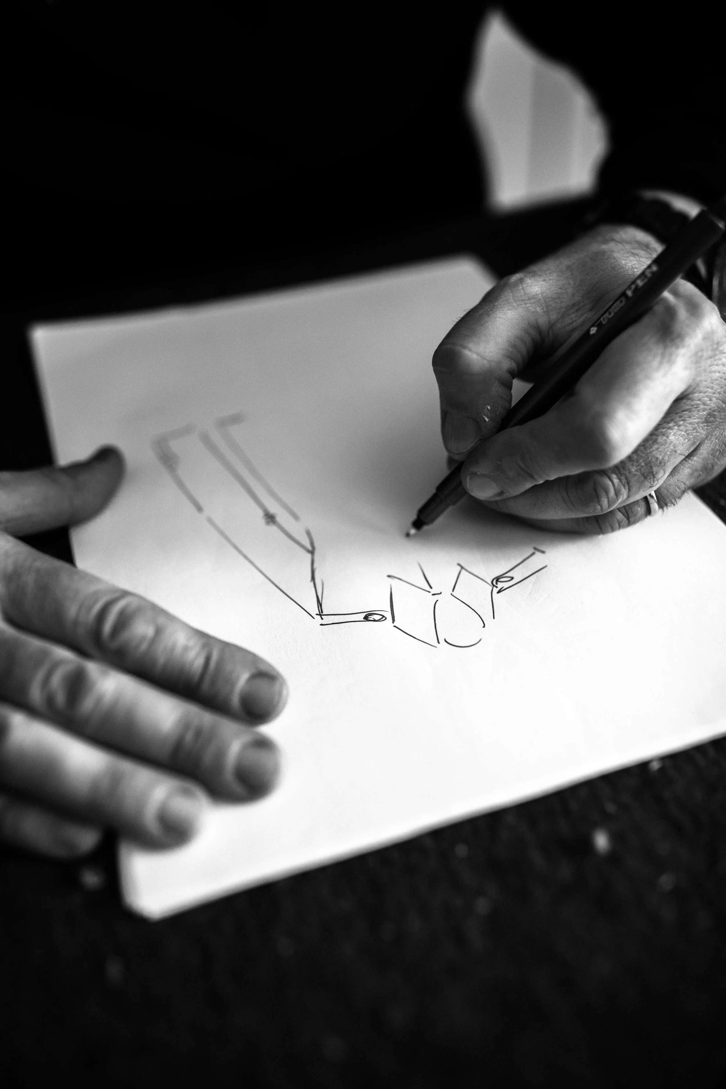 L'immagine mostra una mano che disegna uno schizzo su un foglio di carta, probabilmente di un progetto o di un'idea, in bianco e nero.