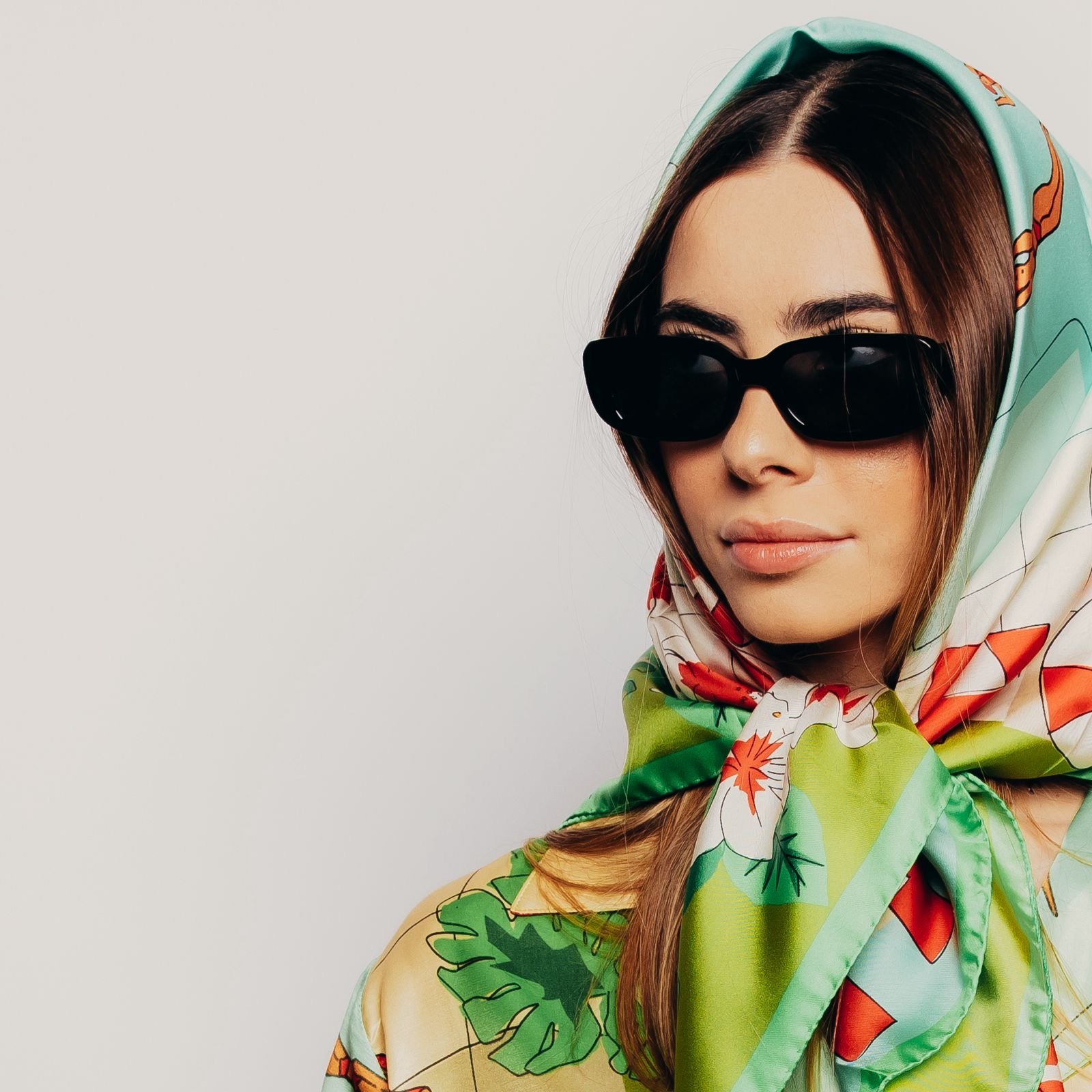 Donna con occhiali da sole neri e foulard colorati con motivi floreali e foglie.