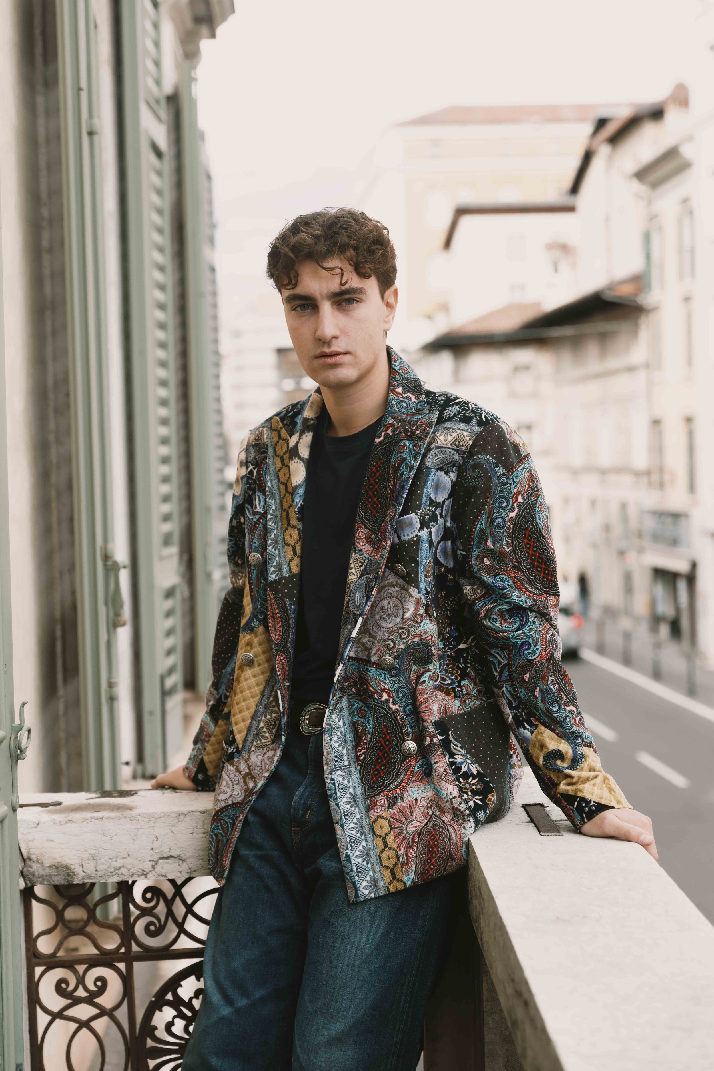 Ragazzo con giacca colorata in un balcone di città, sfondo edificio urbano, giorno.