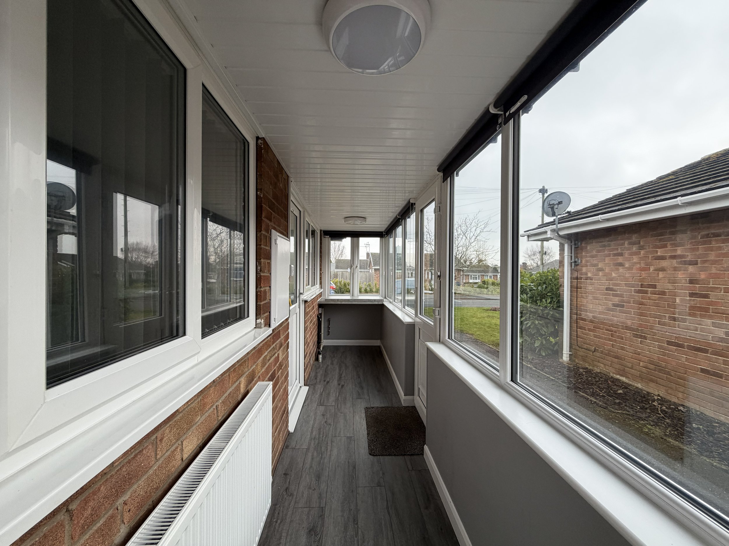  enclosed porch with large windows, brick and painted walls, gray flooring, and a view of the yard outside