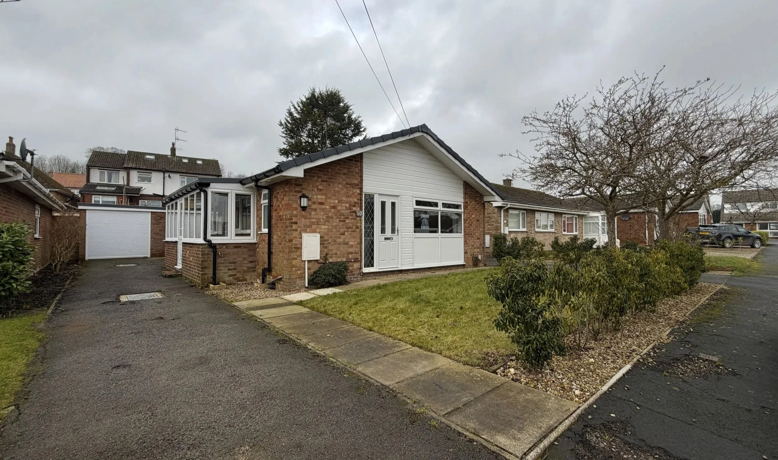 A brick and white siding house with a driveway, a garage, a porch, and a tree in the front yard.