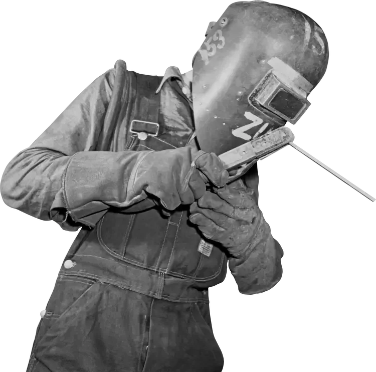 A welder wearing a protective welding mask, gloves, and overalls, using a welding tool.