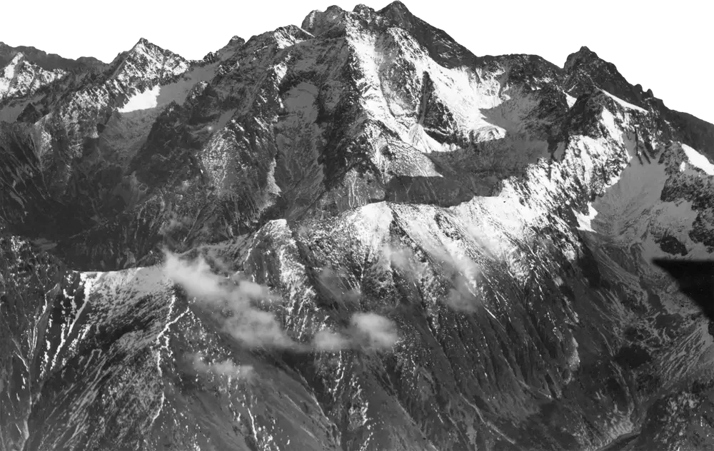 Black and white photograph of a mountain range with snow-covered peaks and rocky ridges.