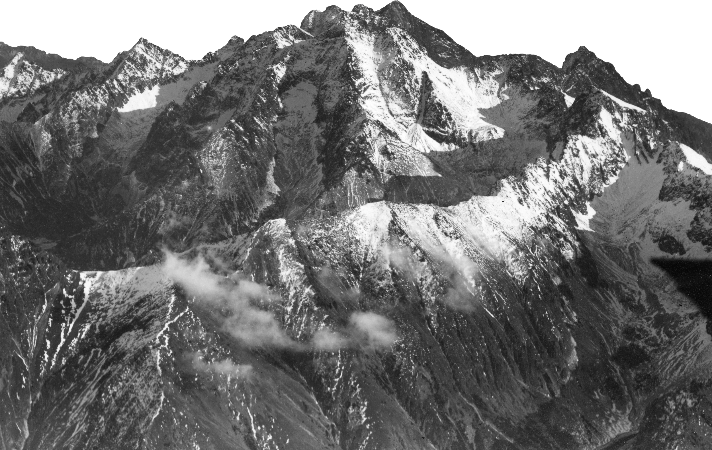 Black and white photograph of a mountain range with snow-covered peaks and rocky ridges.