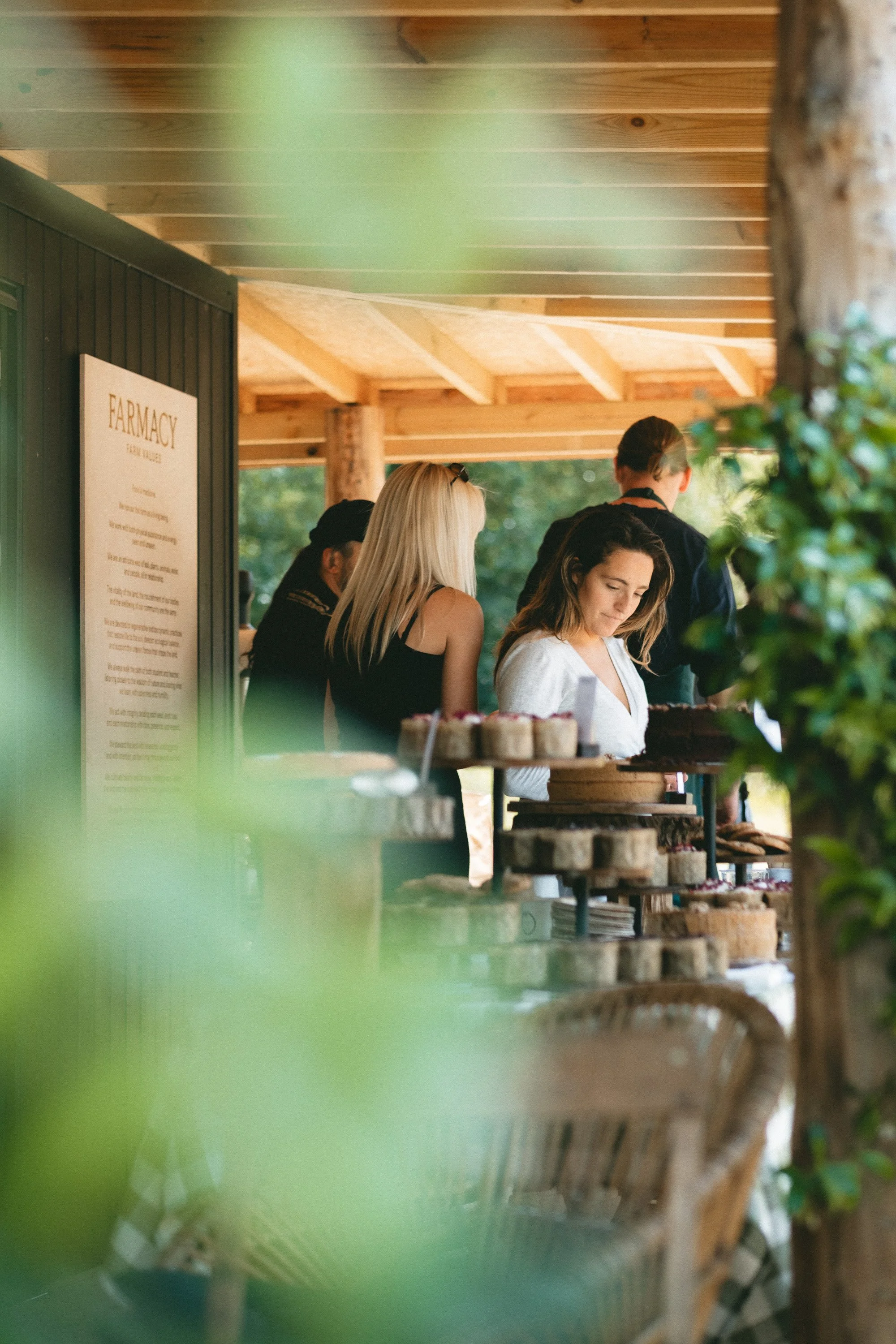 People shopping at a farm store with a sign that reads 'FARMACY' and various jars of products on display.