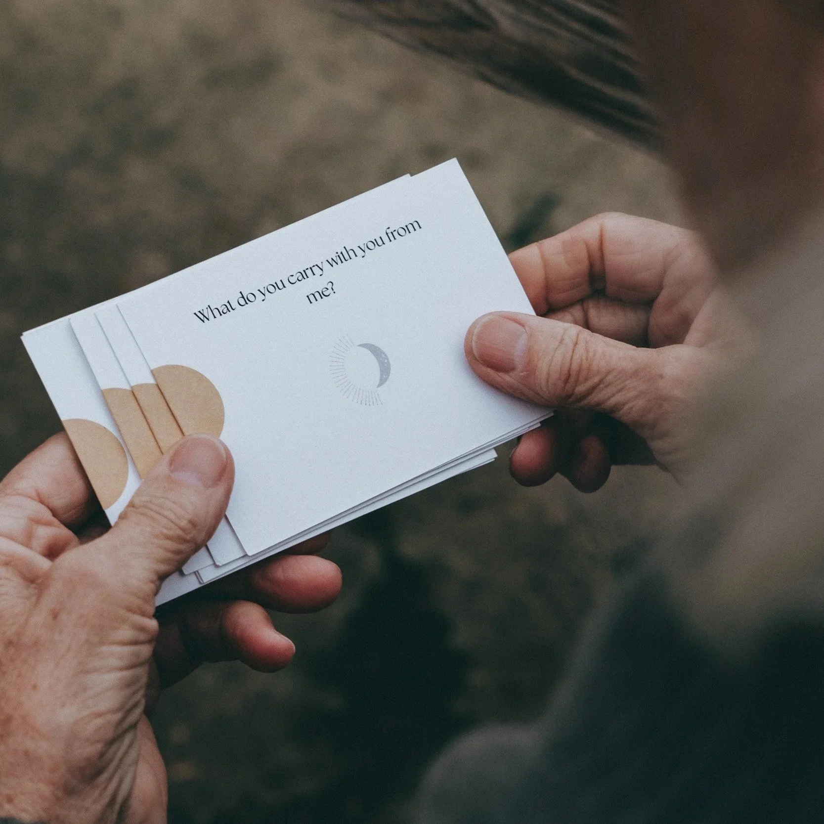 Person holding a stack of cards with the question, 'What do you carry with you from me?' and a moon icon on the top card.