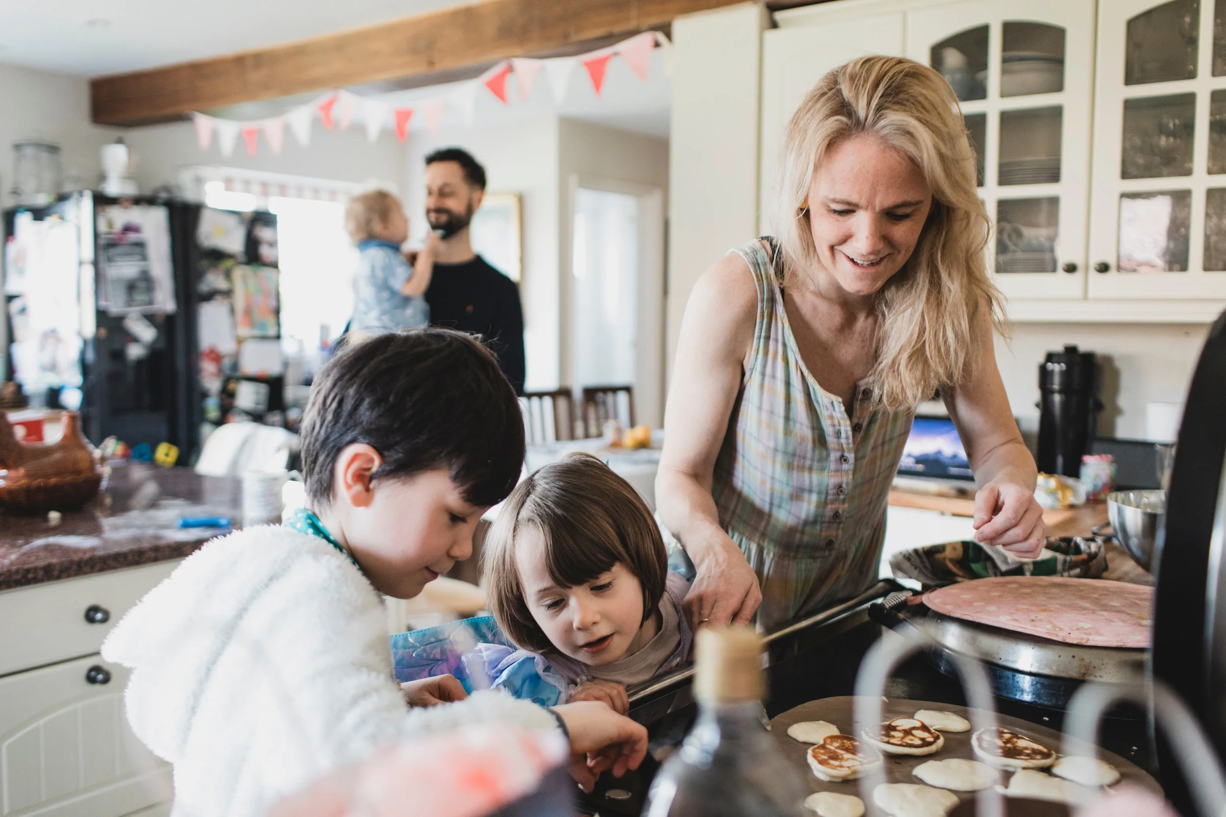 A woman and two children baking cookies in a kitchen, with a man and child in the background.