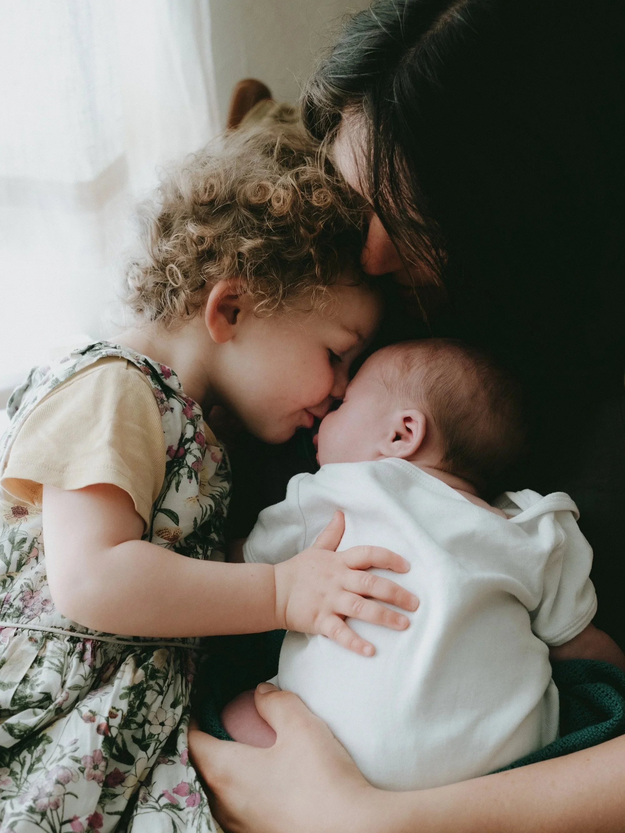 A woman and two young children sharing a close, affectionate moment, with their foreheads touching and eyes closed.
