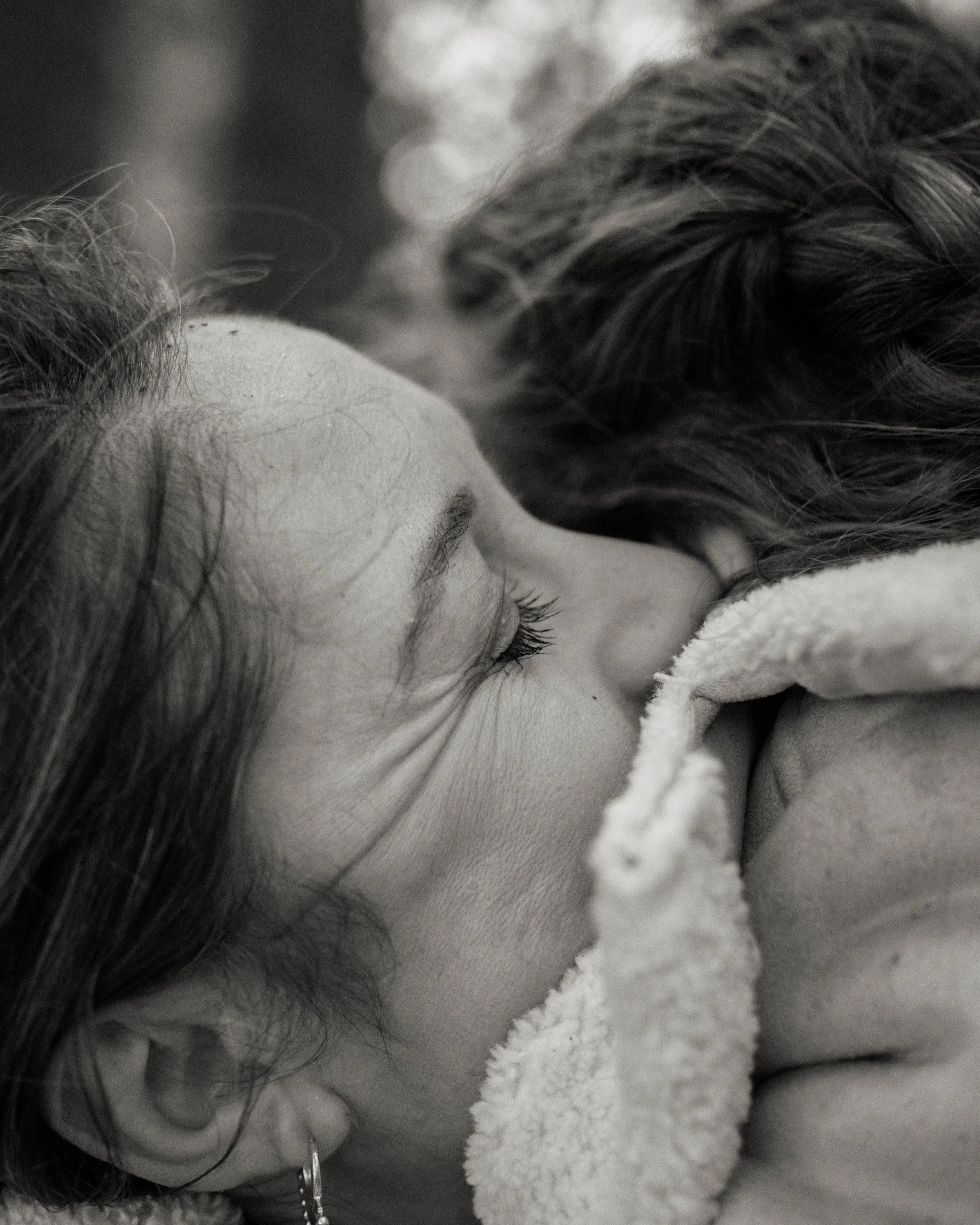 A woman and a child hugging closely, with their faces touching, in a tender moment.
