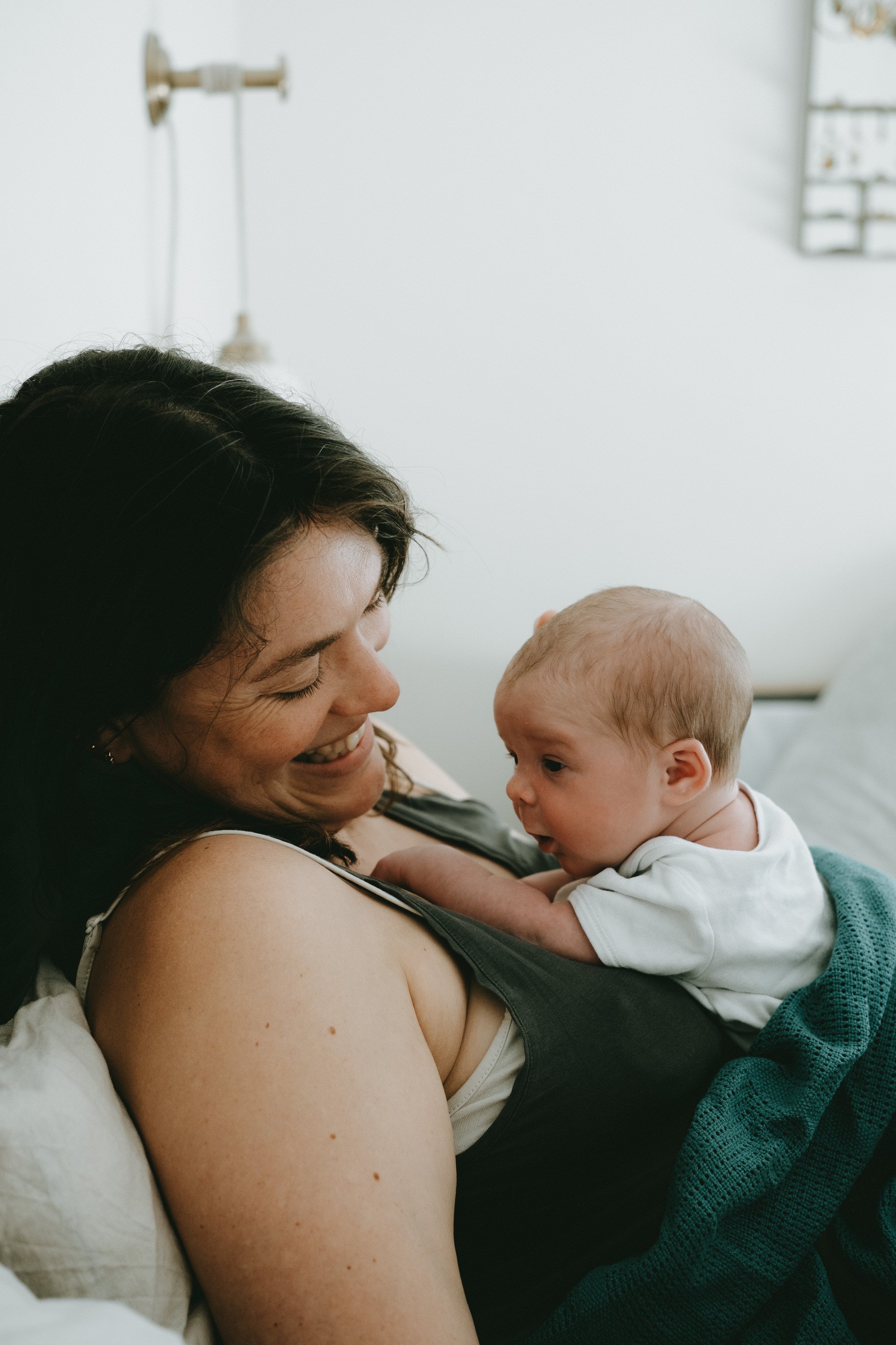 A woman with dark hair smiling at a baby with light hair, who is looking at her.