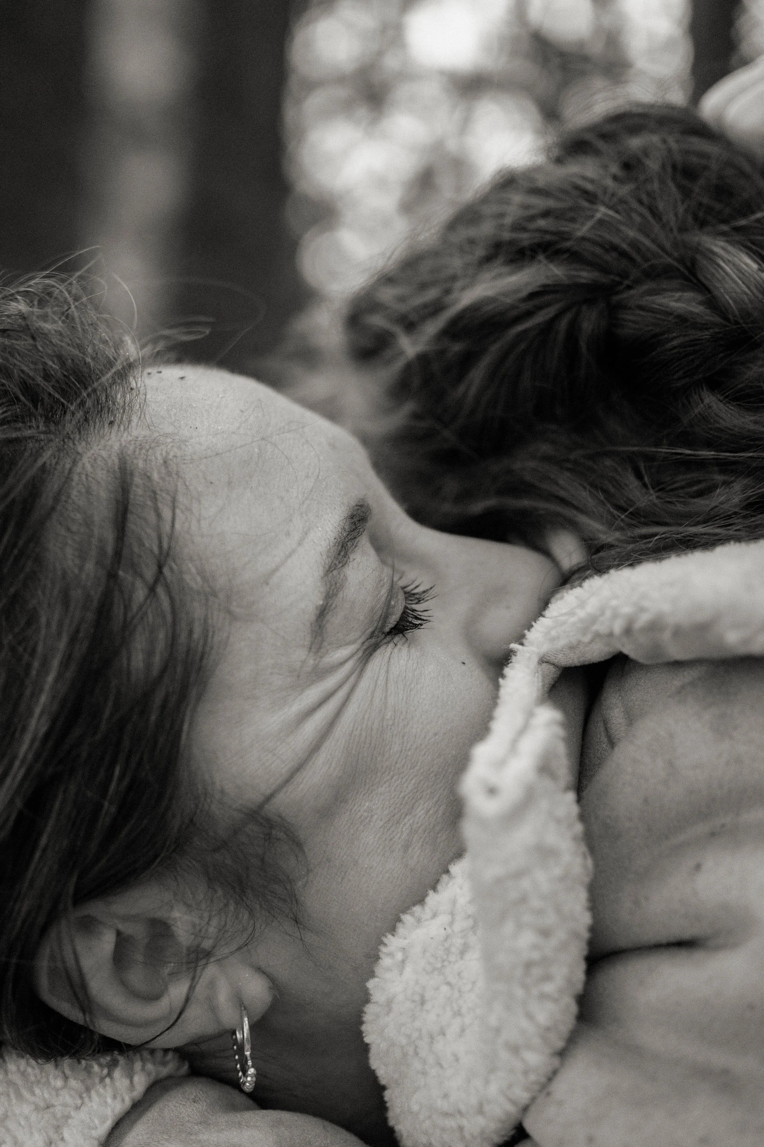 Close-up black and white photo of a person sleeping with a blanket, showing their face, eyelashes, and hair, with another person resting nearby.