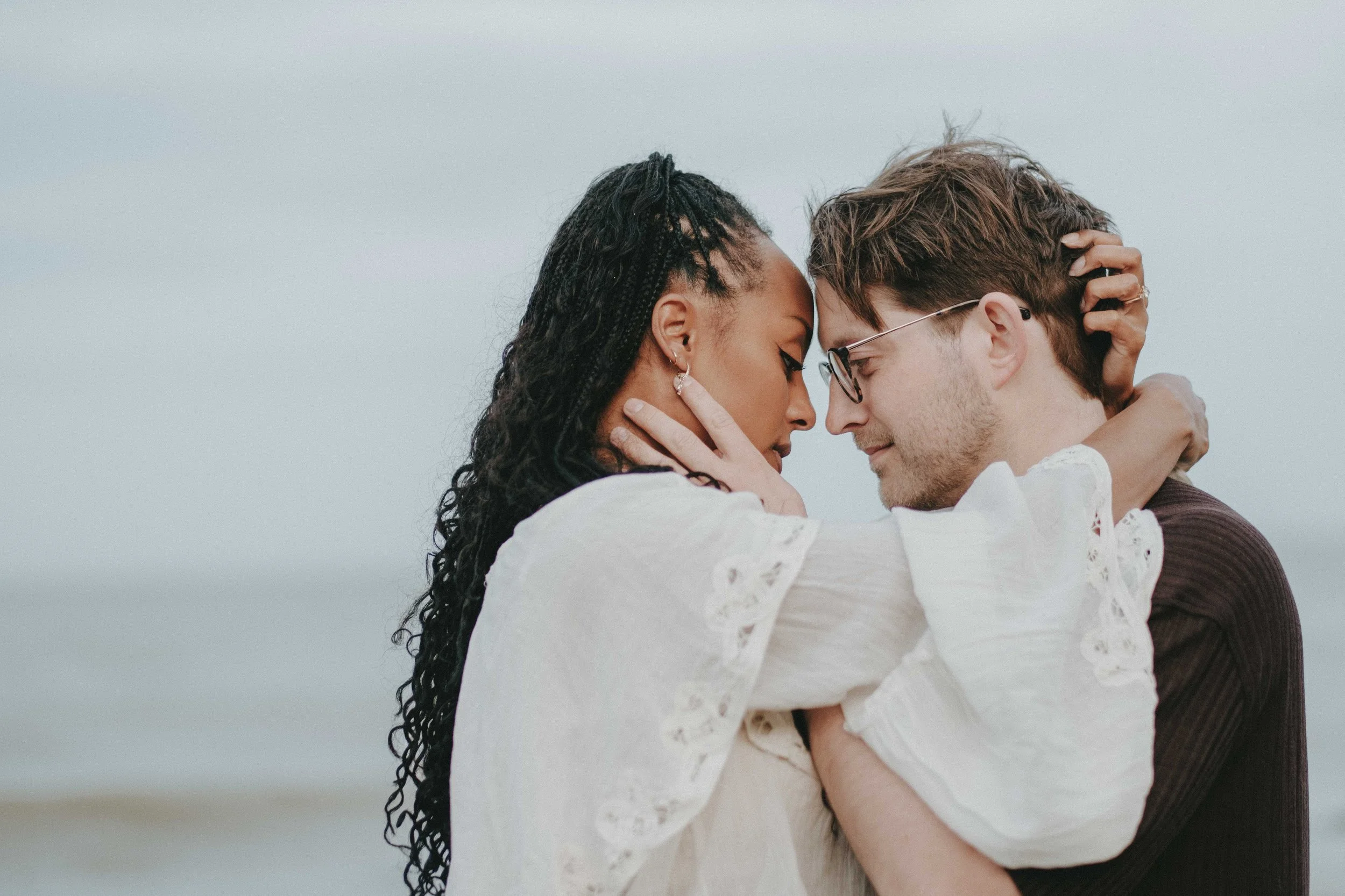 A romantic couple embracing each other on the beach, with their foreheads touching and eyes closed.