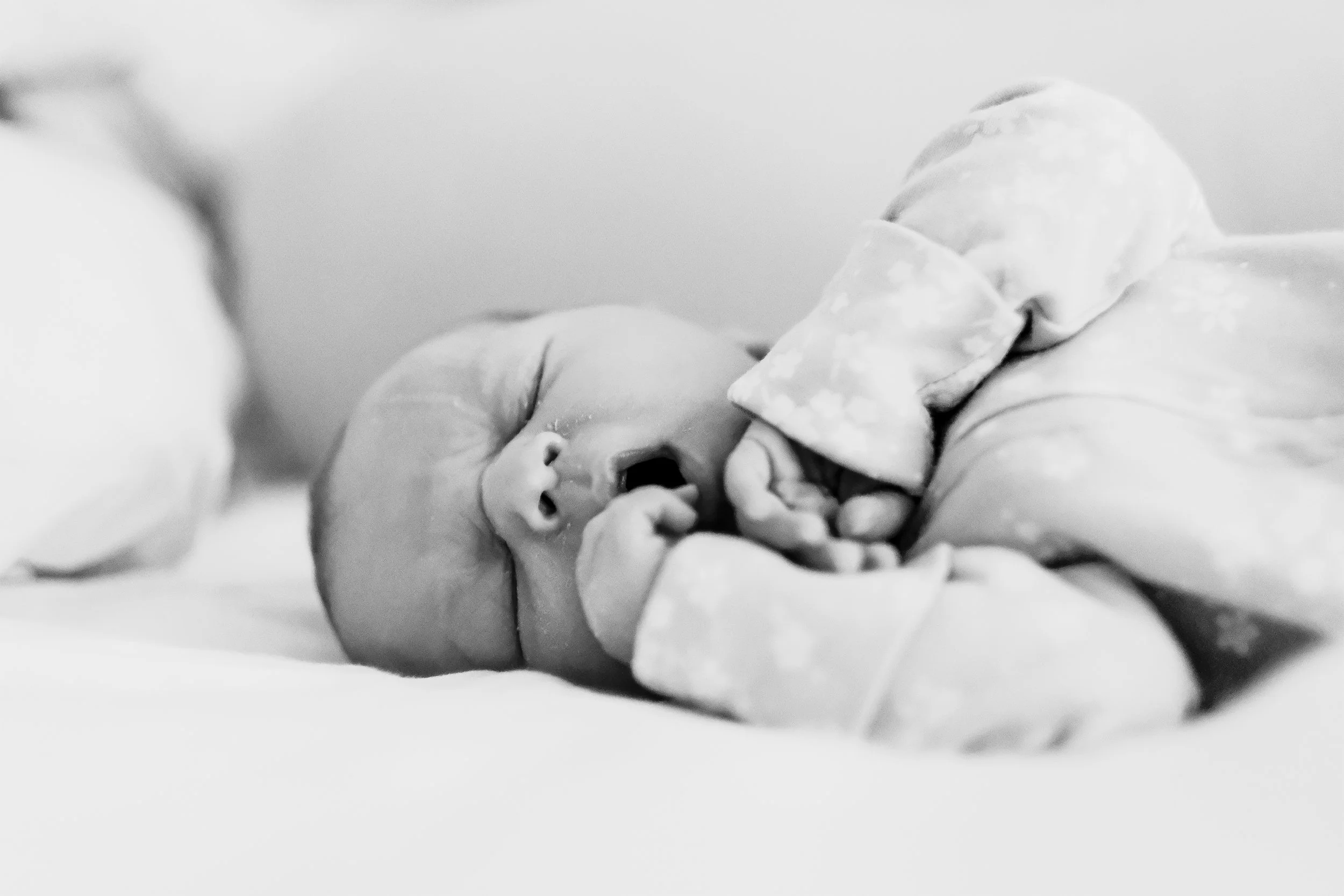 Black and white photo of a newborn baby sleeping, lying on its side with one hand near its face and mouth slightly open.