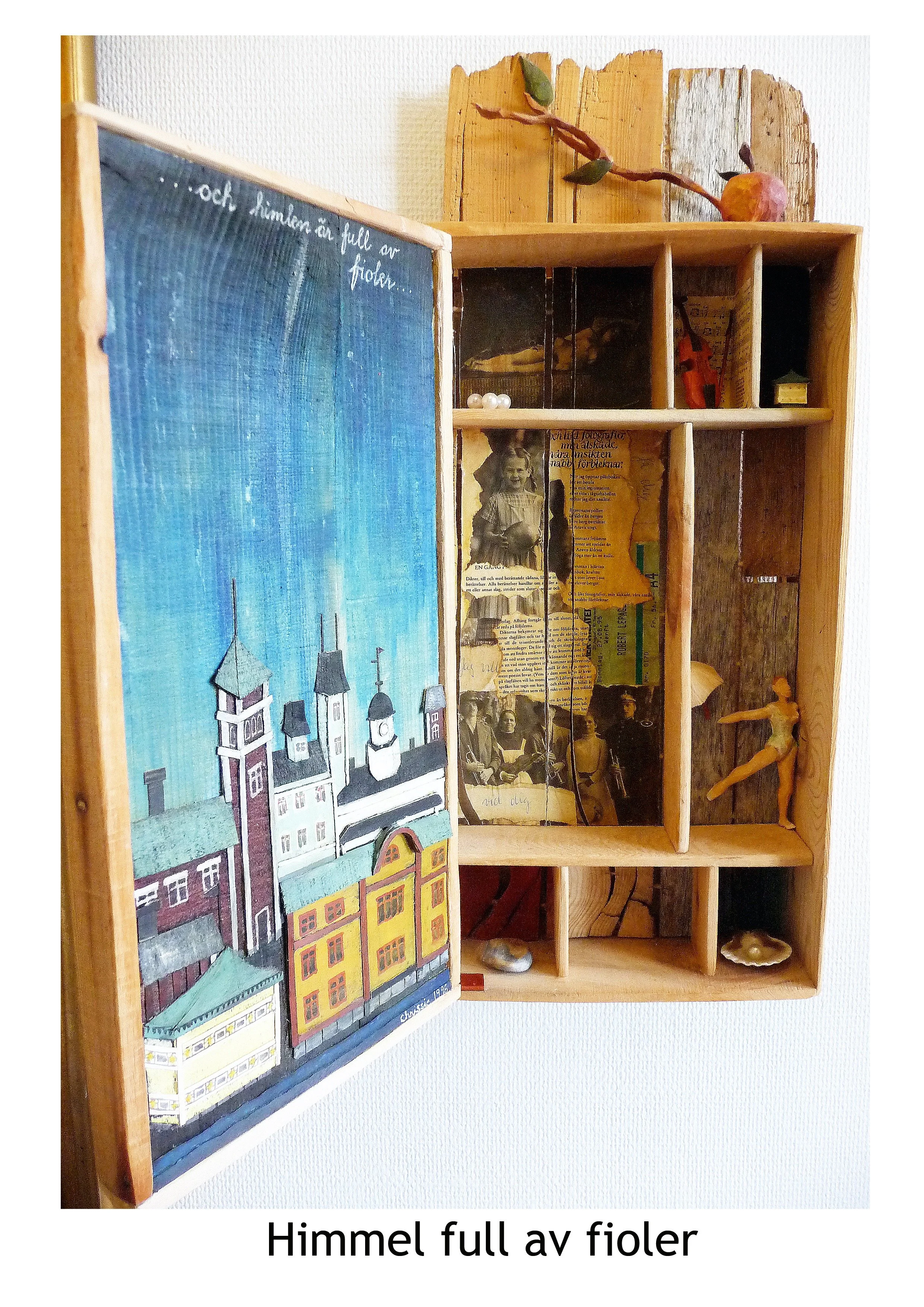 En trähylla med småfack fyllda med olika föremål, inklusive en liten docka, en bild av en äldre kvinna, en spröjd träskulptur av en ballerina, och ett konstverk av en stadssilhuett med blå himmel.