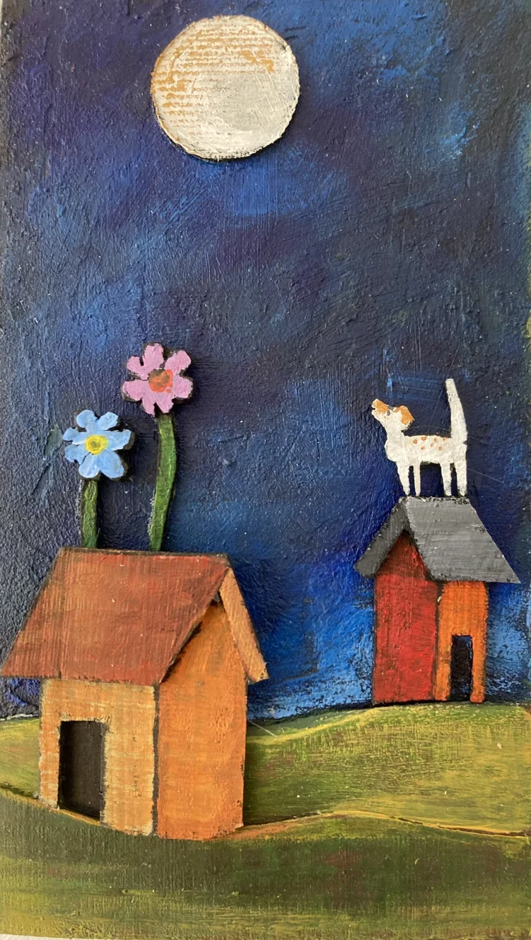 En målning av en nattlig scen med två små hus, varav det ena har två blomsterliknande utsmyckningar på taket och ett kors på, under en stor, rund, ljus måne på en mörkblå himmel. Det finns också en svartvit katt som står på ett av husens tak.