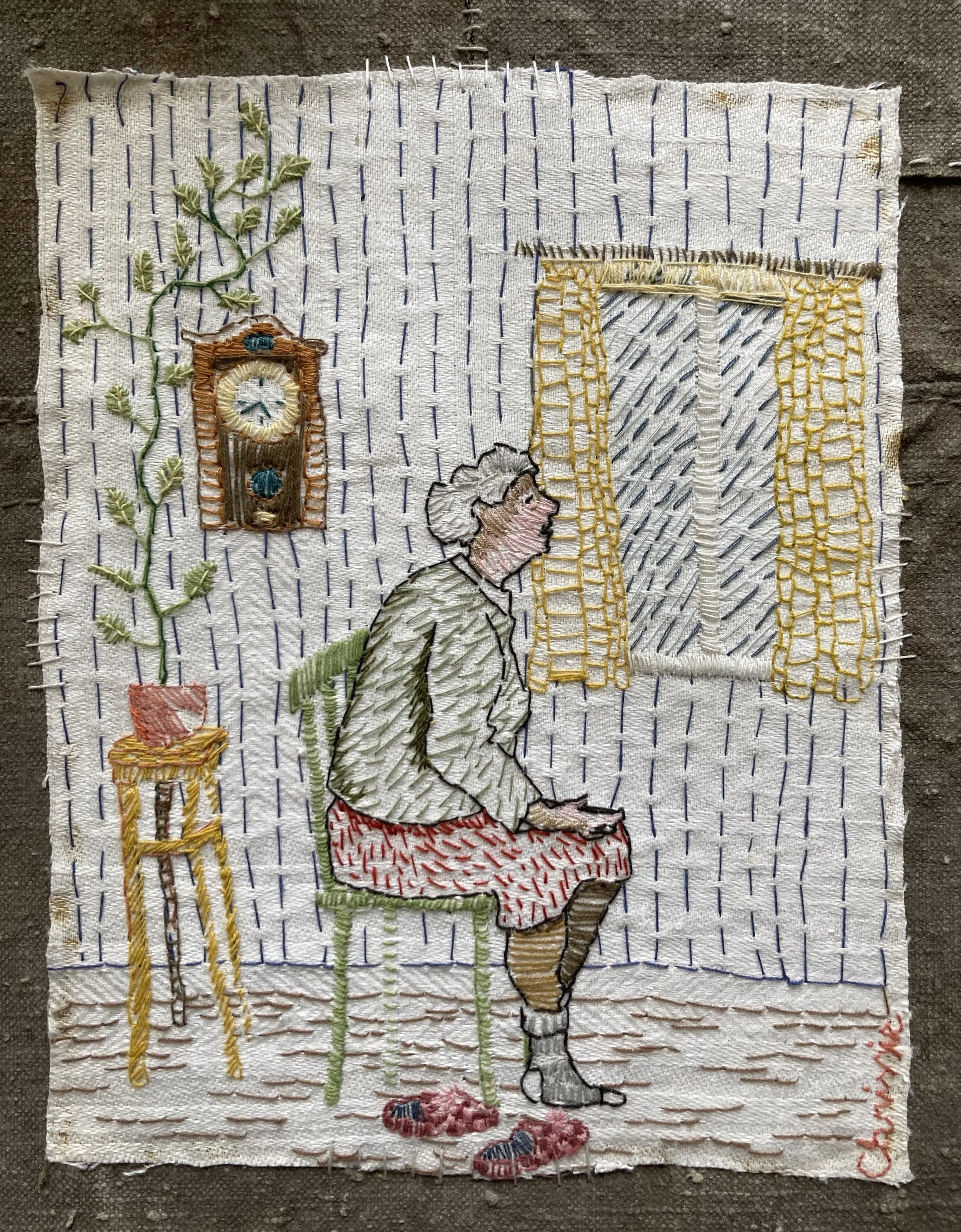 Broderad bild av en kvinna som sitter i ett rum, tittar ut genom ett fönster med gula gardiner. Det finns ett väggur och ett växtställ med en växt, samt ett stolsstativ på golvet. Texten 'Christina' är broderad i det nedre högra hörnet.