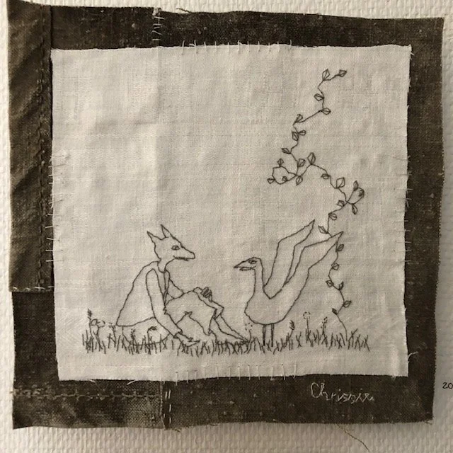 En broderad bild på en räv och en fågel som sitter tillsammans på marken med växtlighet omkring dem.