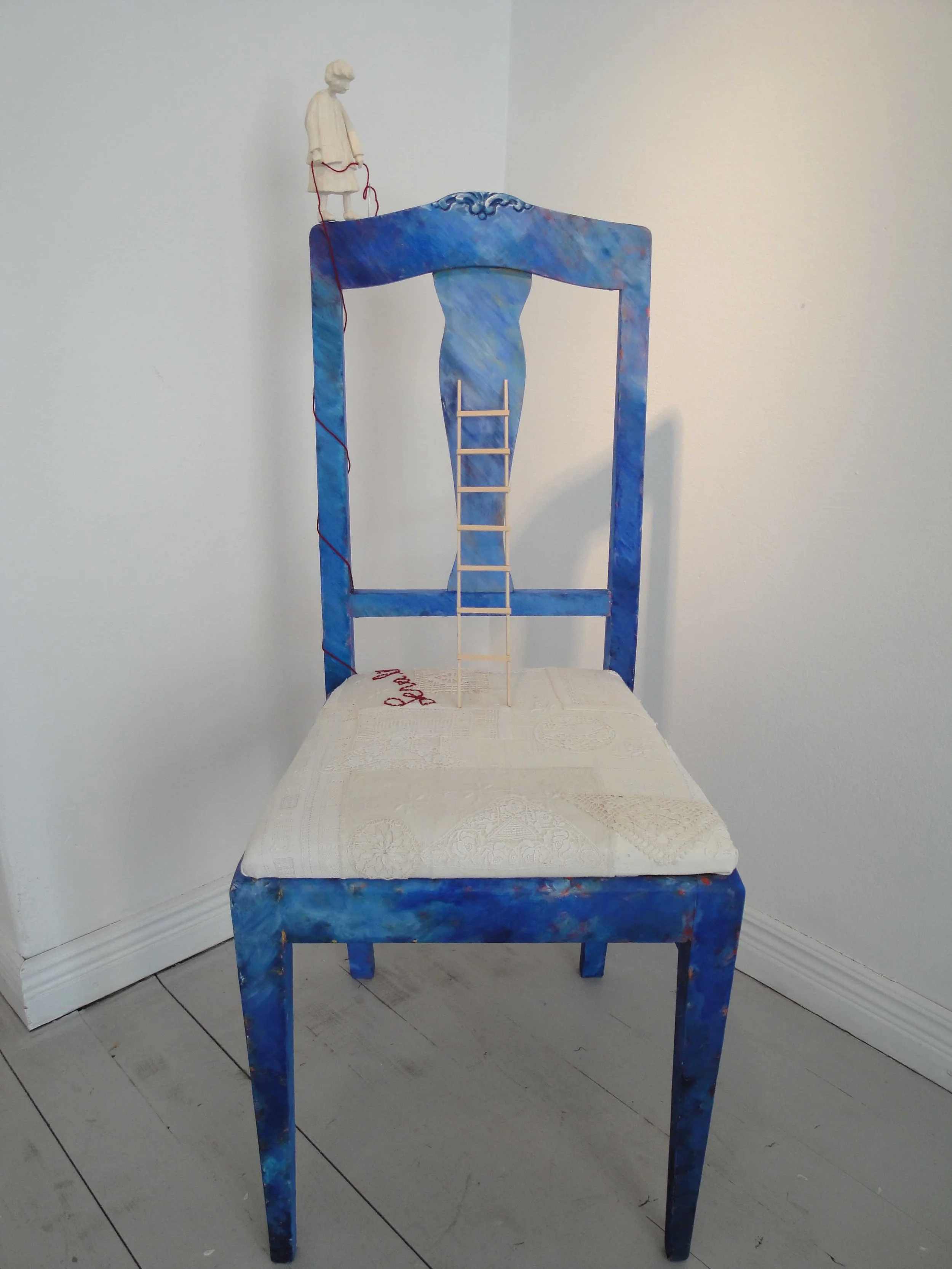 En konstnärlig stol som är målad i olika blå nyanser, med en trappa i mitten och en liten figurin på toppen av ryggstödet.