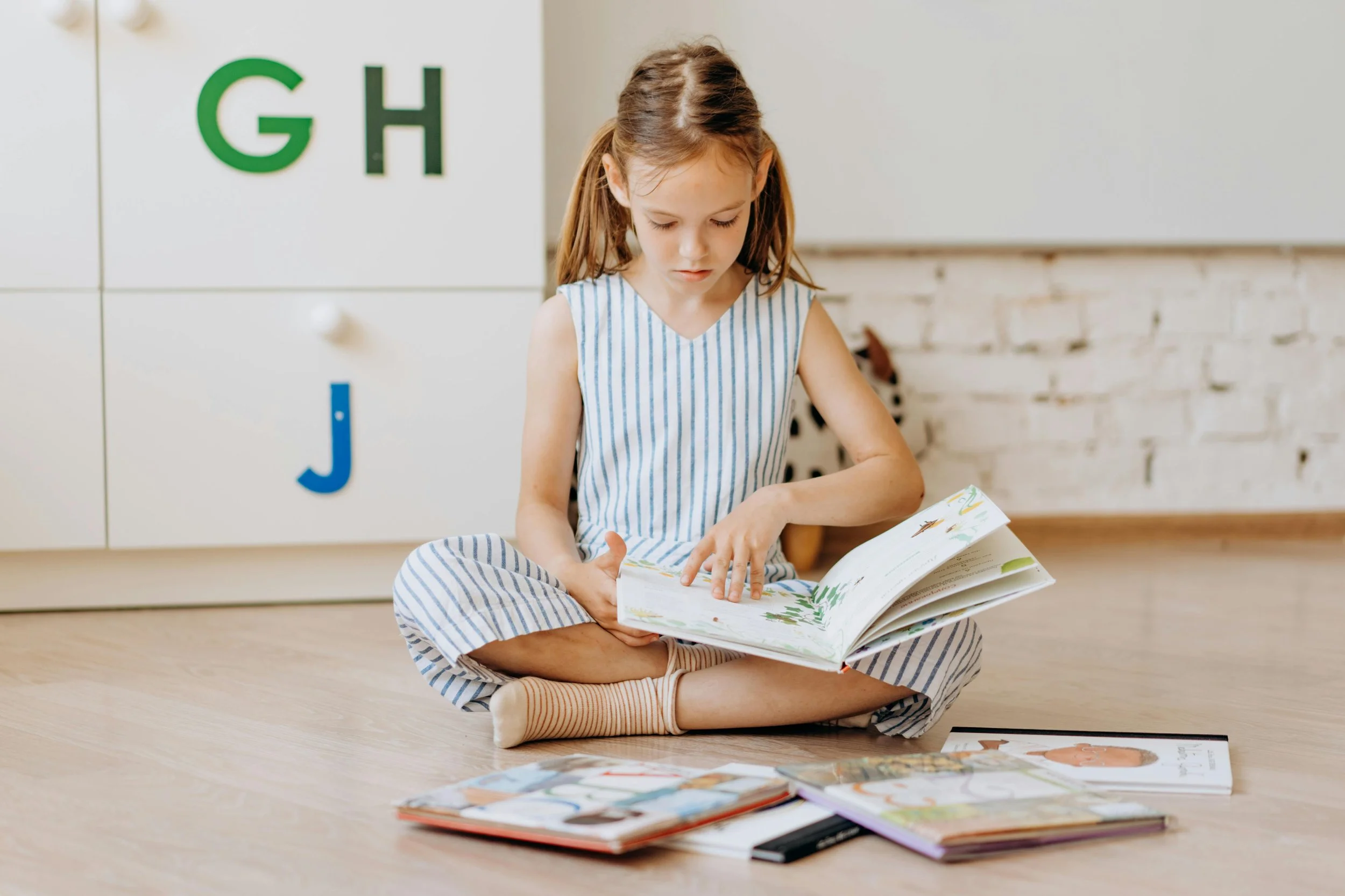 A young girl sitting on the floor reading a book.