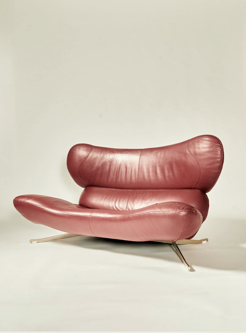 A red leather modern lounge chair with a unique, curved design against a plain light-colored background.